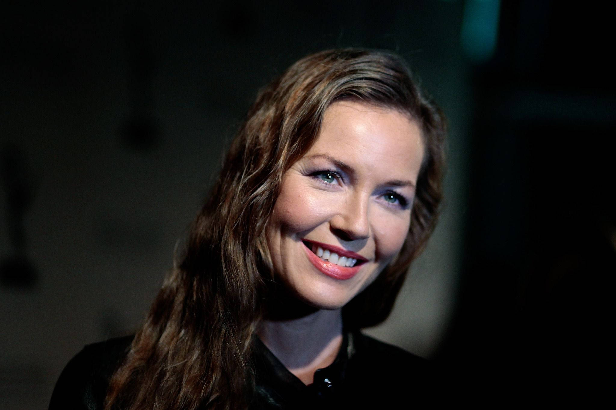 Actress HD 桌布 壁紙 — 一幅溫暖燈光的肖像，一位微笑的長髮棕眼女性，背景為黑暗模糊。