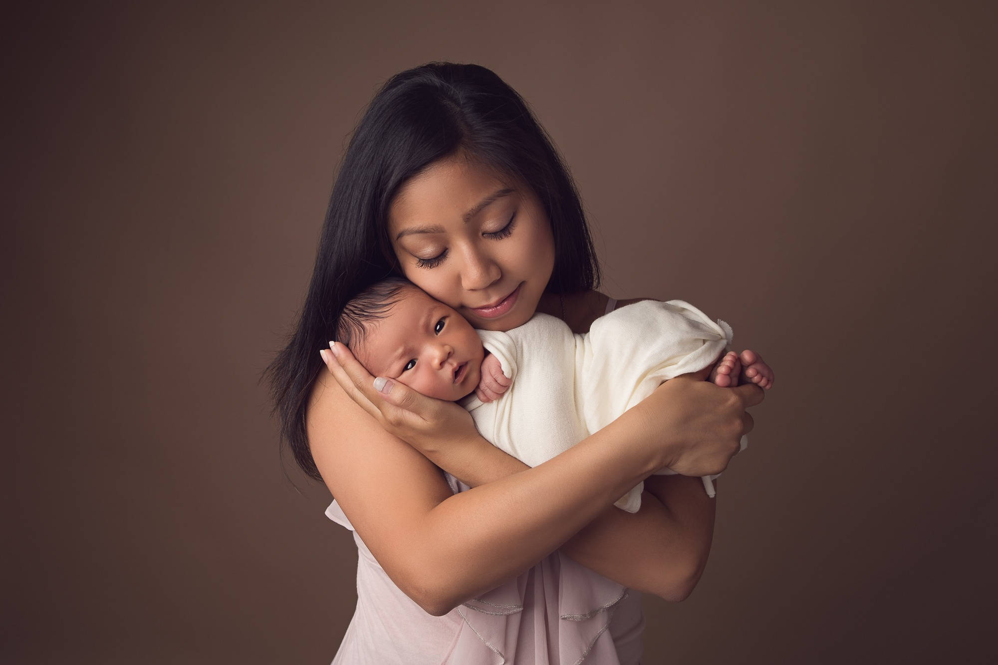 Mother And Baby 桌布 壁紙 — 一幅溫柔的肖像，母親在柔軟的棕色背景下懷抱著她的新生嬰兒。