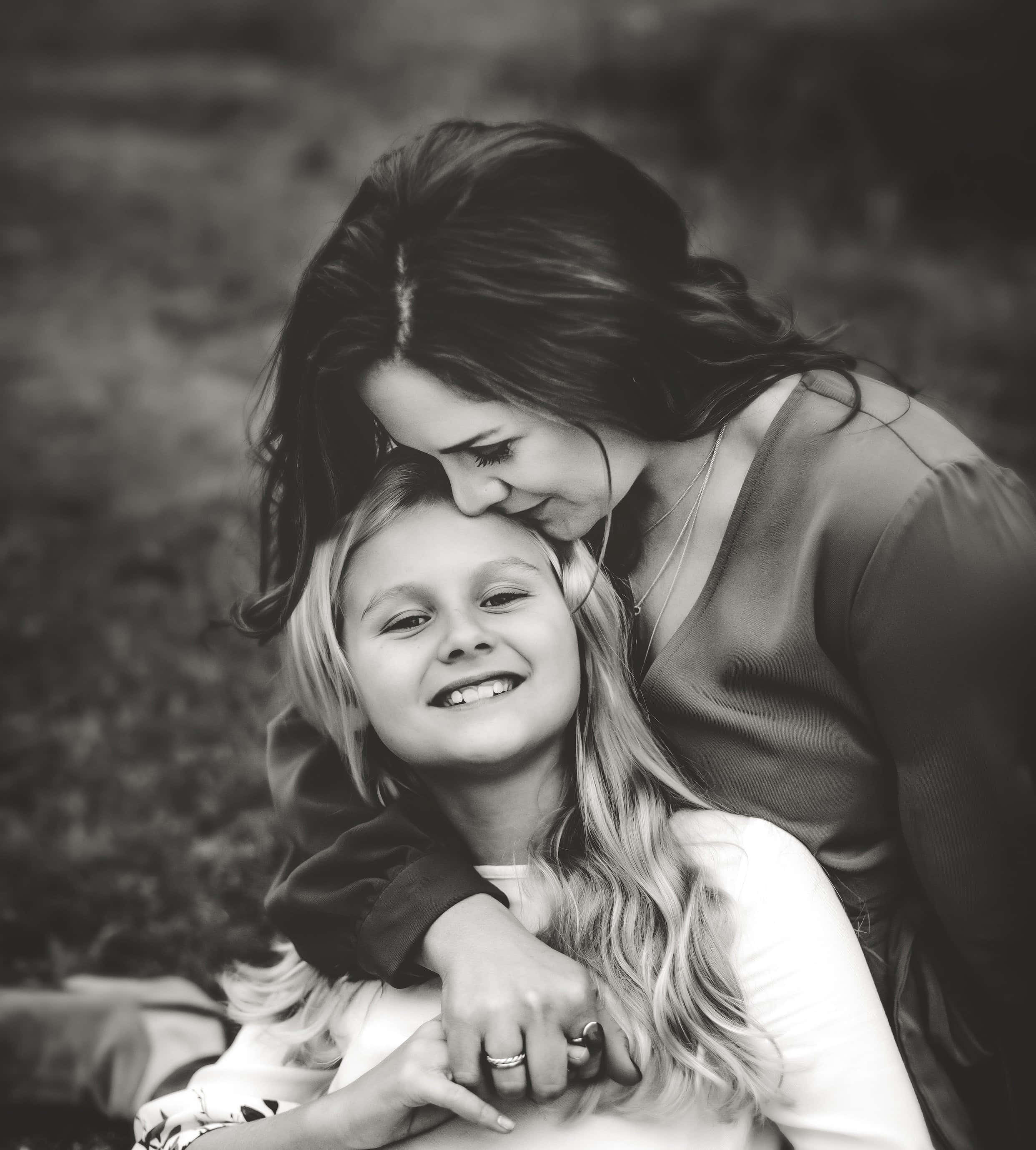 Mother Love 桌布 壁紙 — 一幅溫柔的黑白肖像，一位女性在戶外環境中輕輕地用鼻子蹭著微笑的女兒的額頭。