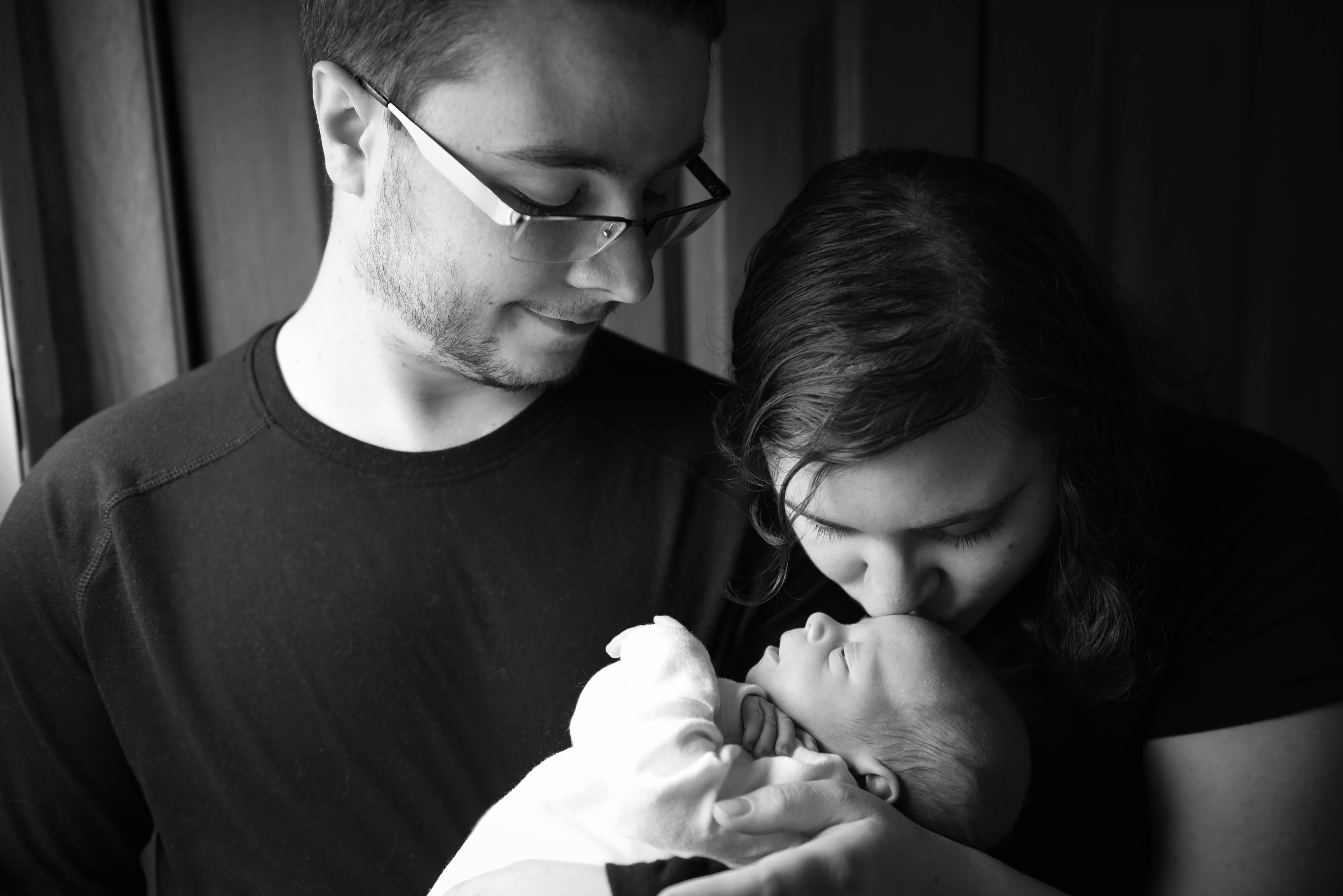 Mom 桌布 壁紙 — 一幅溫柔的黑白肖像，父母輕輕抱著並親吻他們的新生嬰兒。