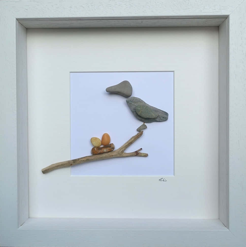 Pebble Art 桌布 壁紙 — 一幅用光滑石頭和浮木製成的裱框藝術品，描繪了一隻棲息在樹枝上的鳥，下方有兩個鳥蛋。