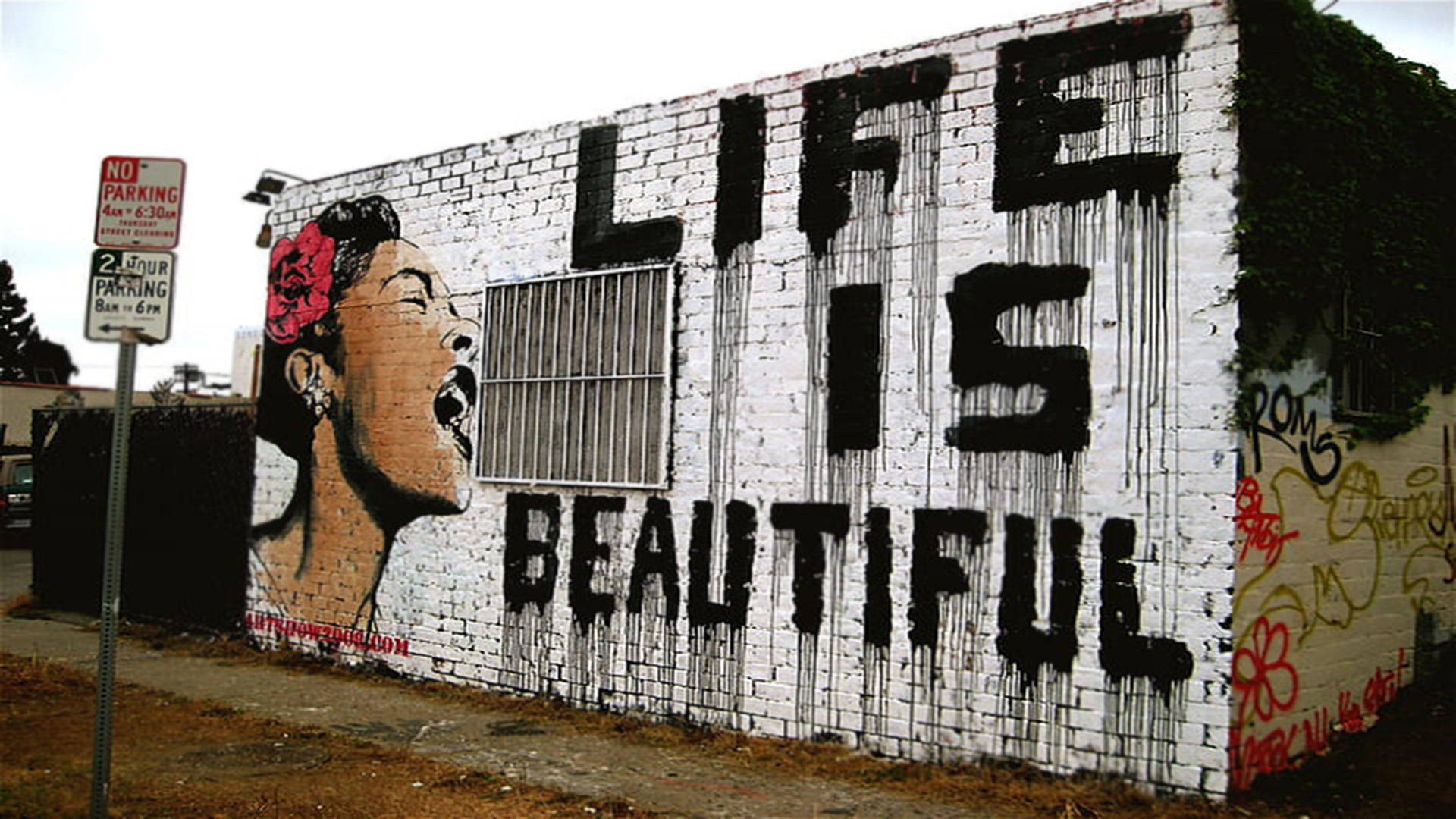 Banksy 桌布 壁紙 — 一幅白色磚牆上的大膽塗鴉壁畫描繪了一個頭髮上插著紅玫瑰的女人，用滴落的黑色字母尖叫著「生命是美麗的」這句話。