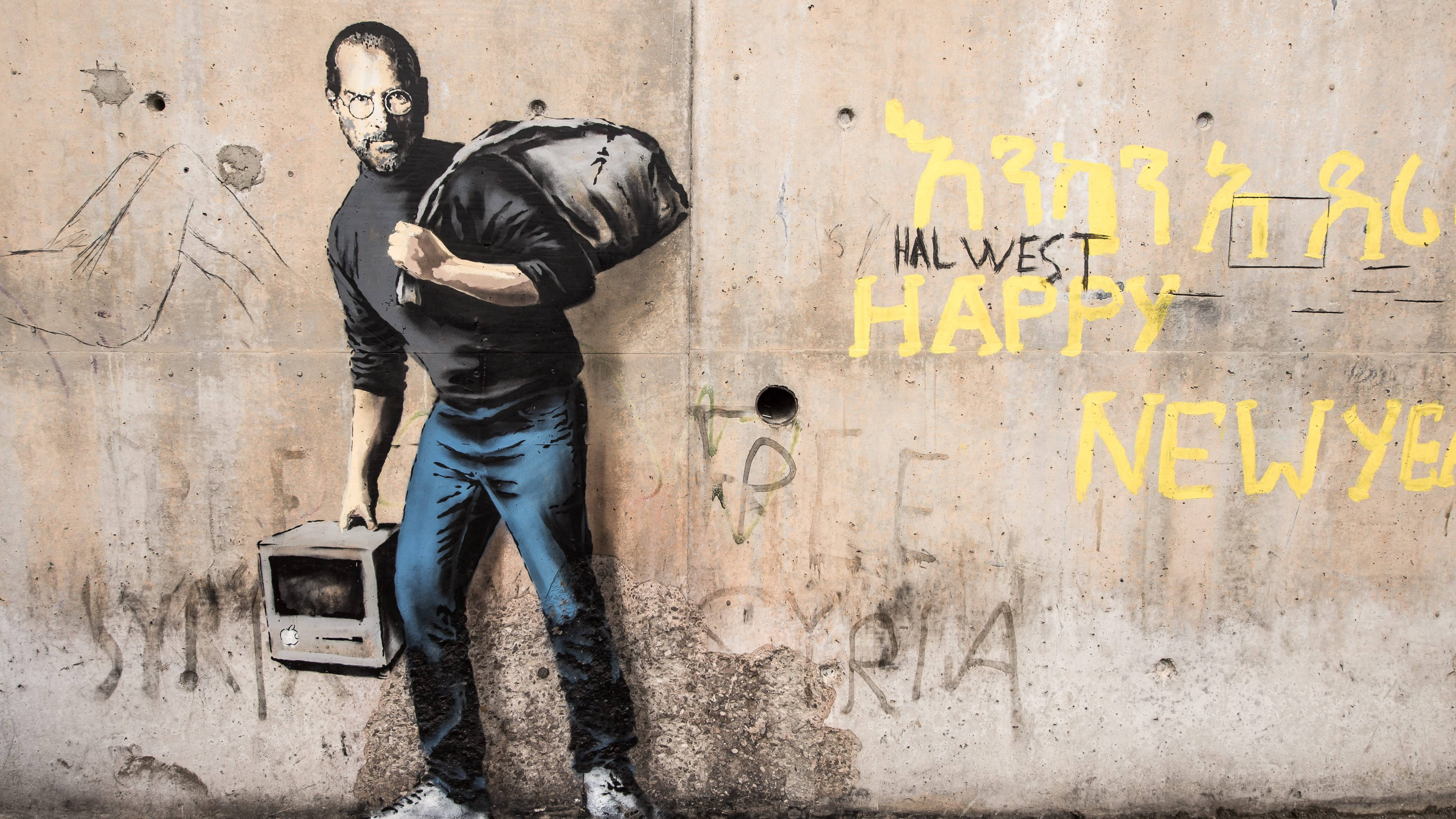 Banksy 桌布 壁紙 — 一幅粗獷的街頭壁畫，描繪一名穿著高領毛衣的男子，背著一個麻袋，並拿著一台舊電視，背景是佈滿塗鴉的混凝土牆。