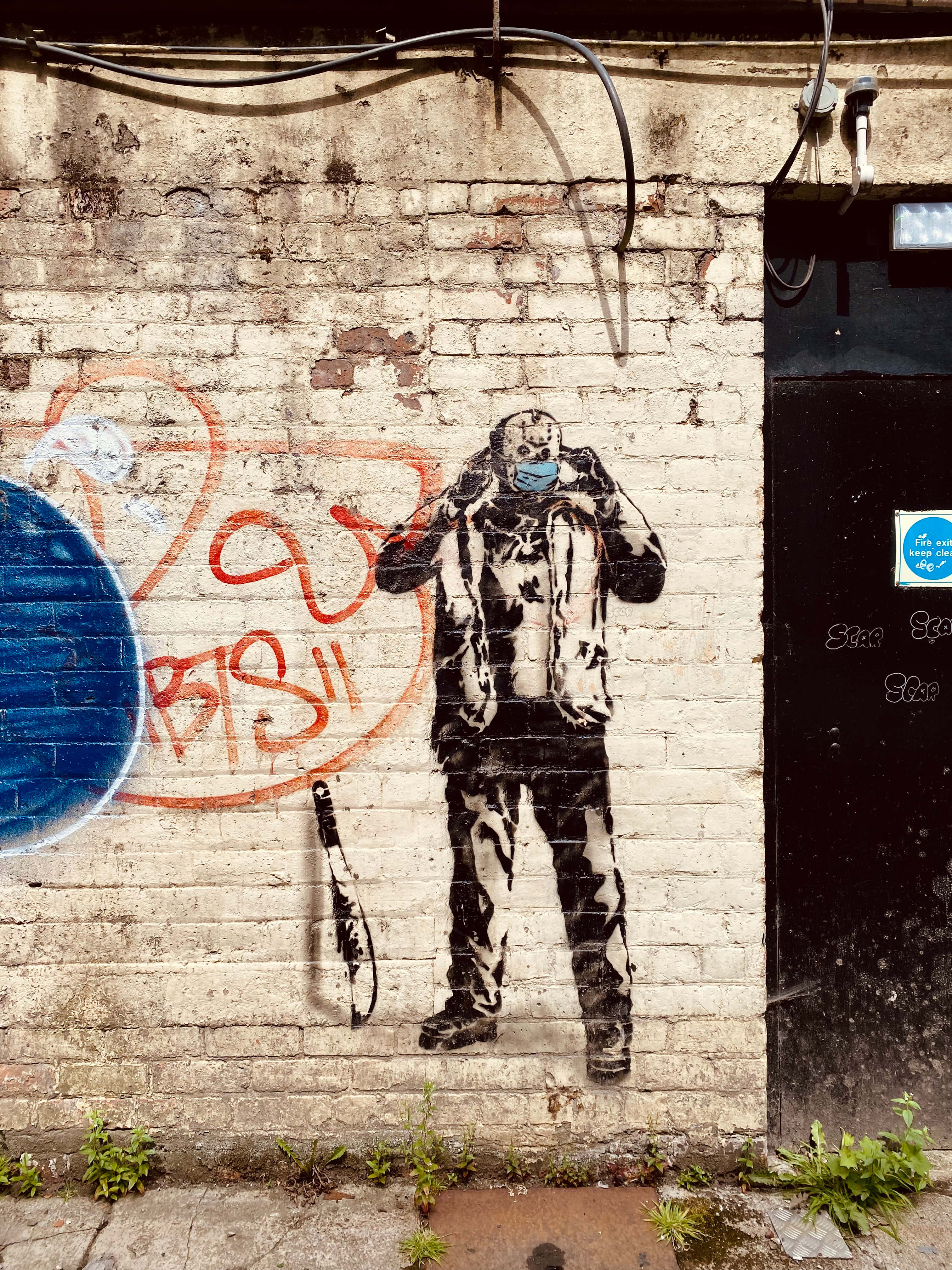 Spray Paint 桌布 壁紙 — 一幅粗糙的街頭壁畫描繪一個戴面具的人物，在藍色圓圈和橙色塗鴉旁邊拿著一把刀，背景是風化的磚牆。