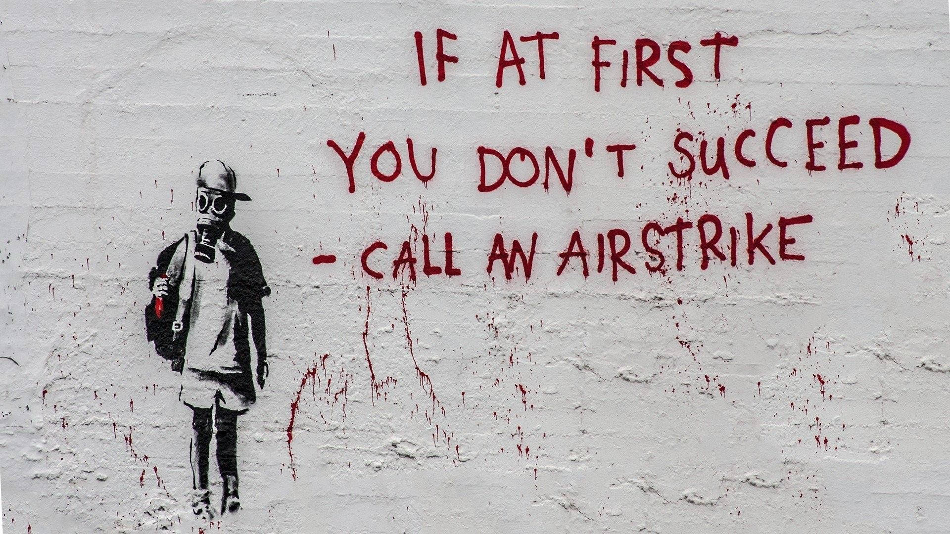 Banksy 桌布 壁紙 — 一幅粗糙的街頭藝術壁畫顯示一個戴著防毒面具的小孩拿著玩具槍，旁邊有粗體紅色塗鴉文字寫著「IF AT FIRST YOU DON'T SUCCEED - CALL AN AIRSTRIKE」。
