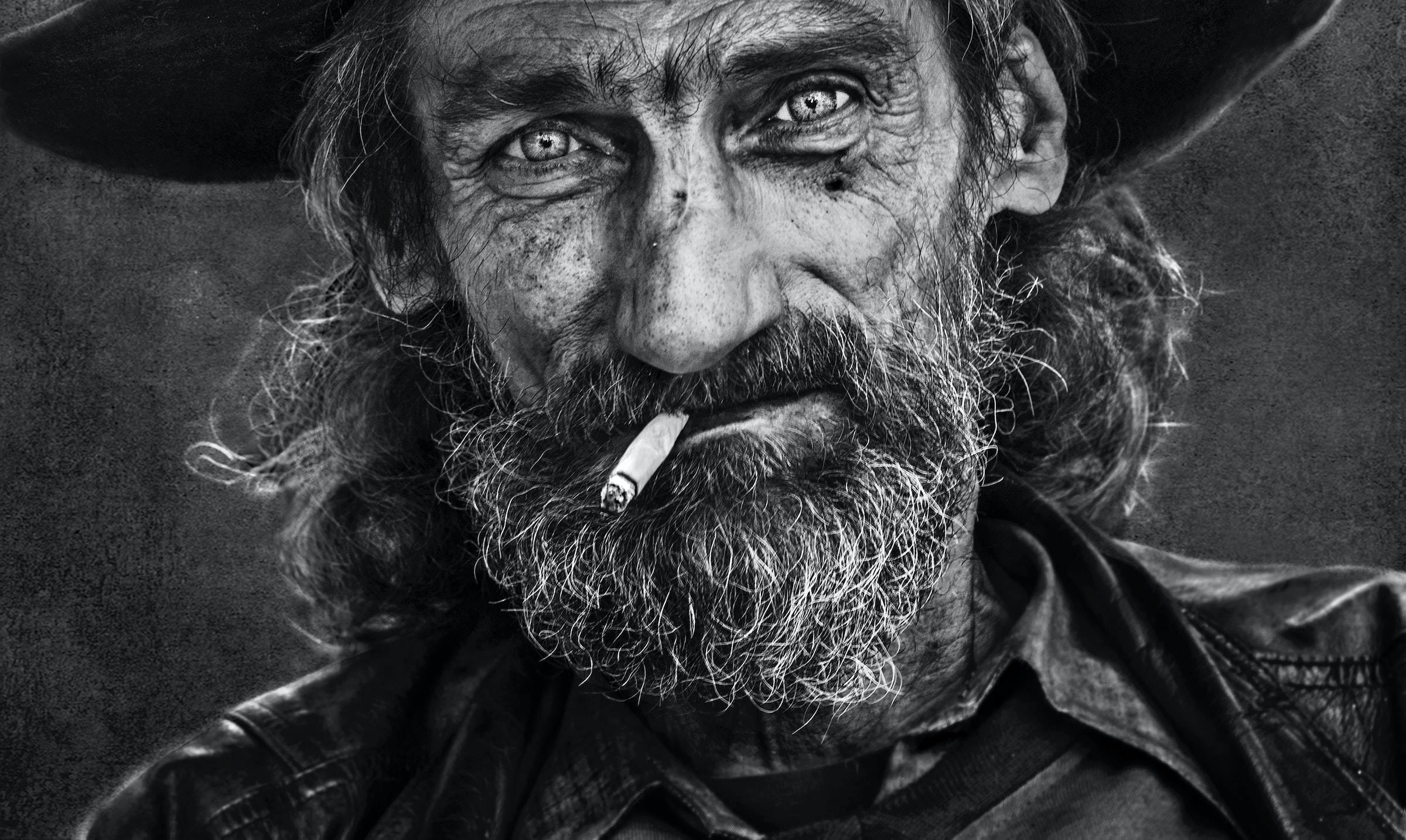 Black And White Portrait 桌布 壁紙 — 一幅粗糙的黑白肖像，描繪一個飽經風霜的男人，鬍子裡叼著香煙，戴著寬邊帽。