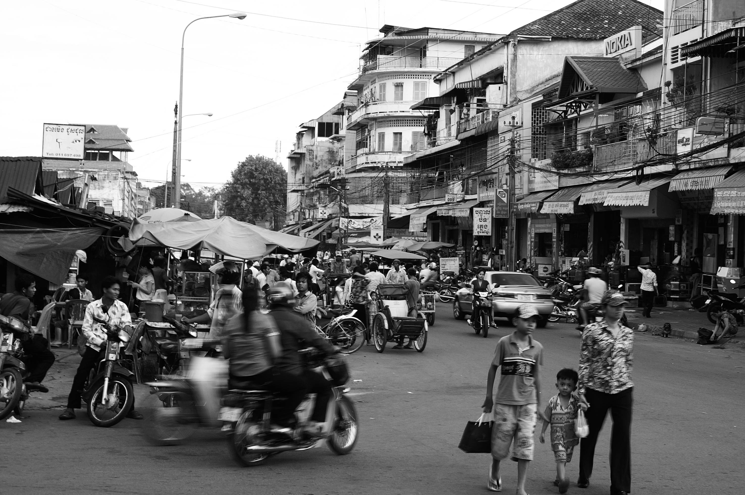 Cambodia 桌布 壁紙 — 一幅繁忙的黑白街景，機車和行人穿梭於擁擠的城市小巷。