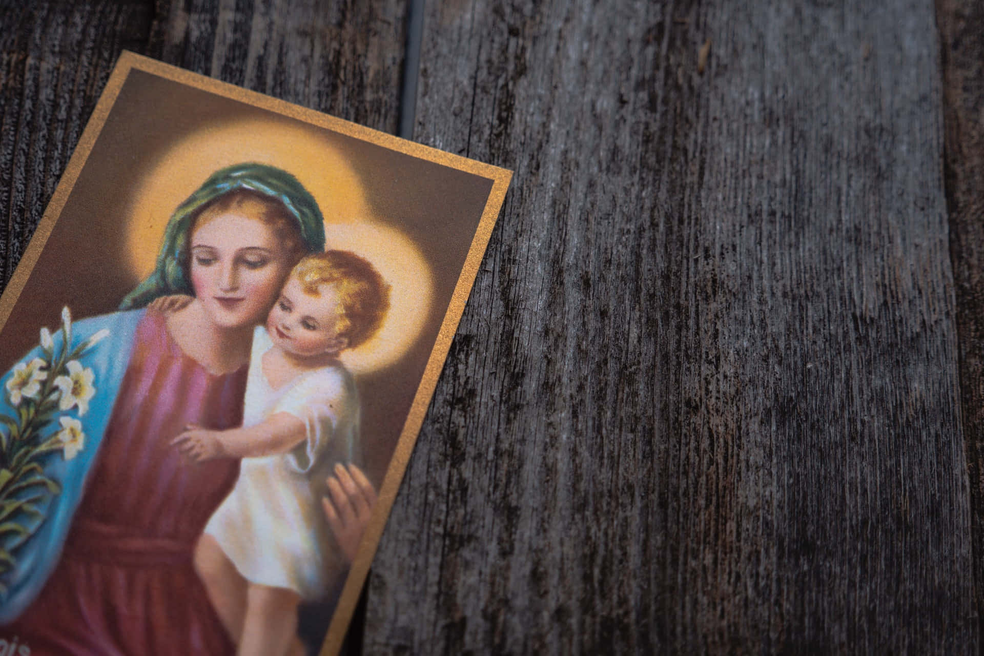 Mother Mary 桌布 壁紙 — 一幅聖母瑪利亞懷抱嬰兒耶穌的復古宗教版畫，置於風化的深色木頭上，帶有柔和的金色光環。