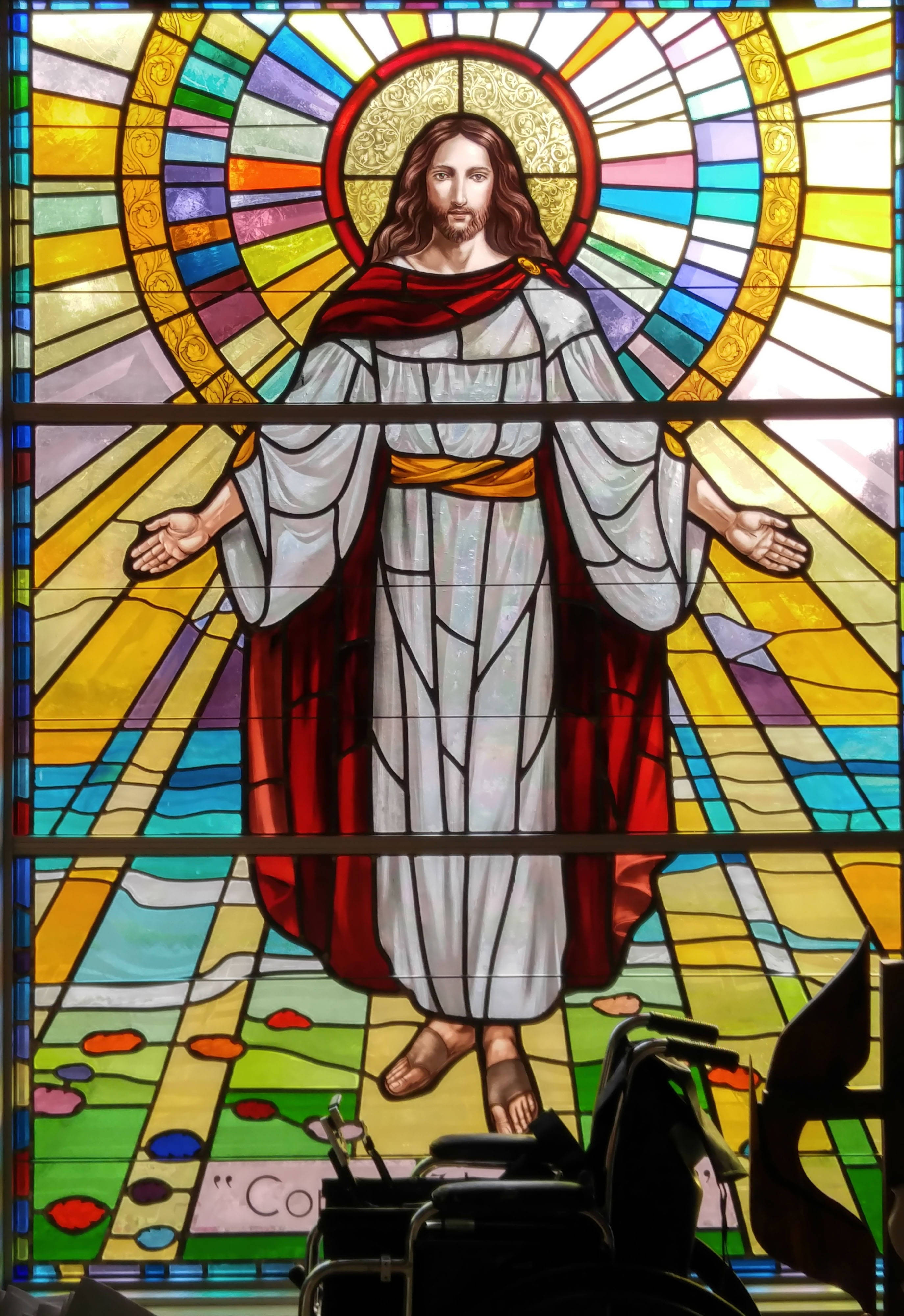 Christ 桌布 壁紙 — 一幅色彩鮮豔的彩繪玻璃窗描繪耶穌基督張開雙臂，帶有光環，背景是色彩繽紛的幾何圖案。