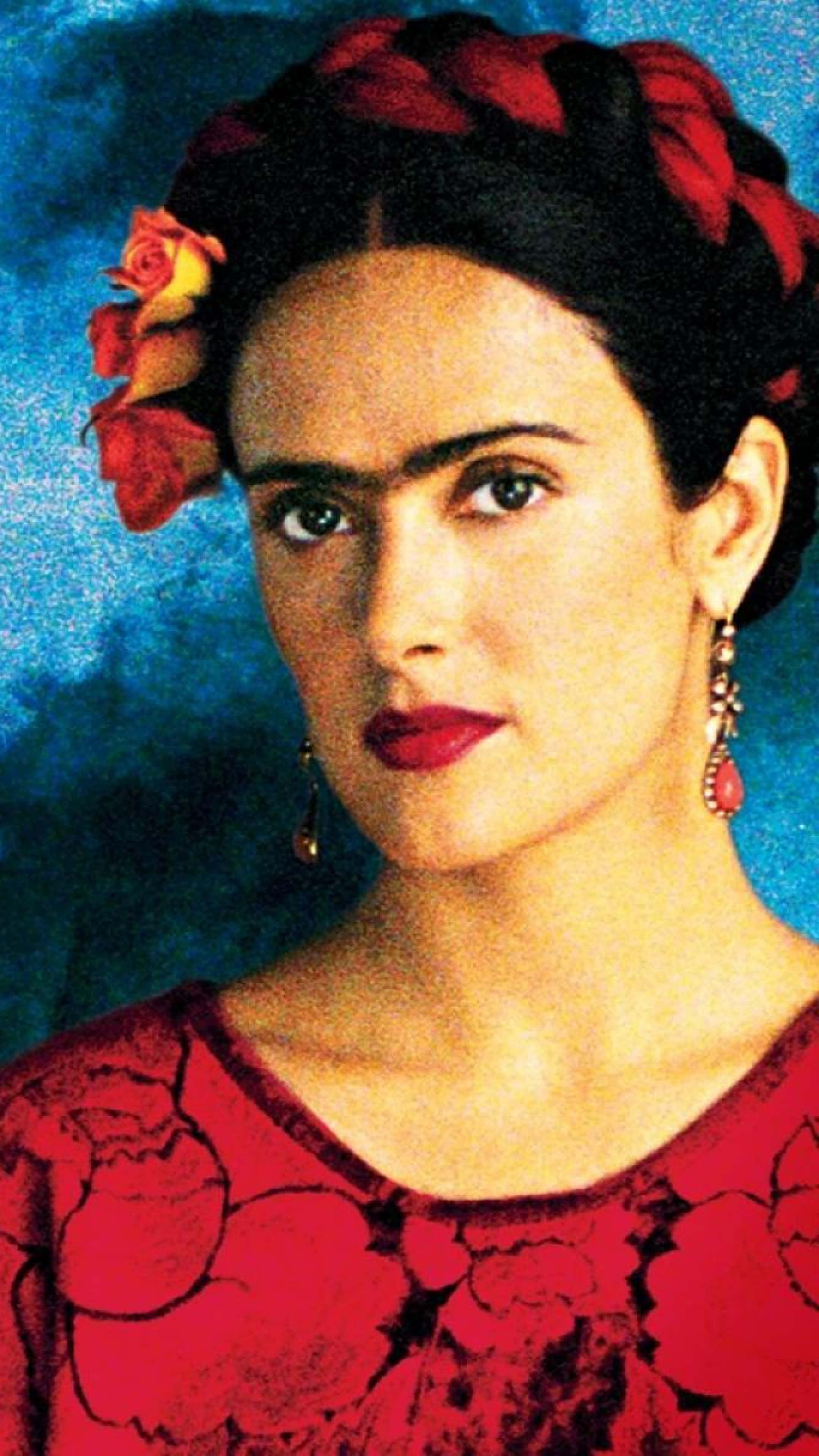 Frida Kahlo 桌布 壁紙 — 一幅芙烈達·卡蘿的肖像，深色辮子頭髮飾以紅玫瑰，身穿紅色花卉連衣裙和垂墜耳環，背景為有紋理的藍色。