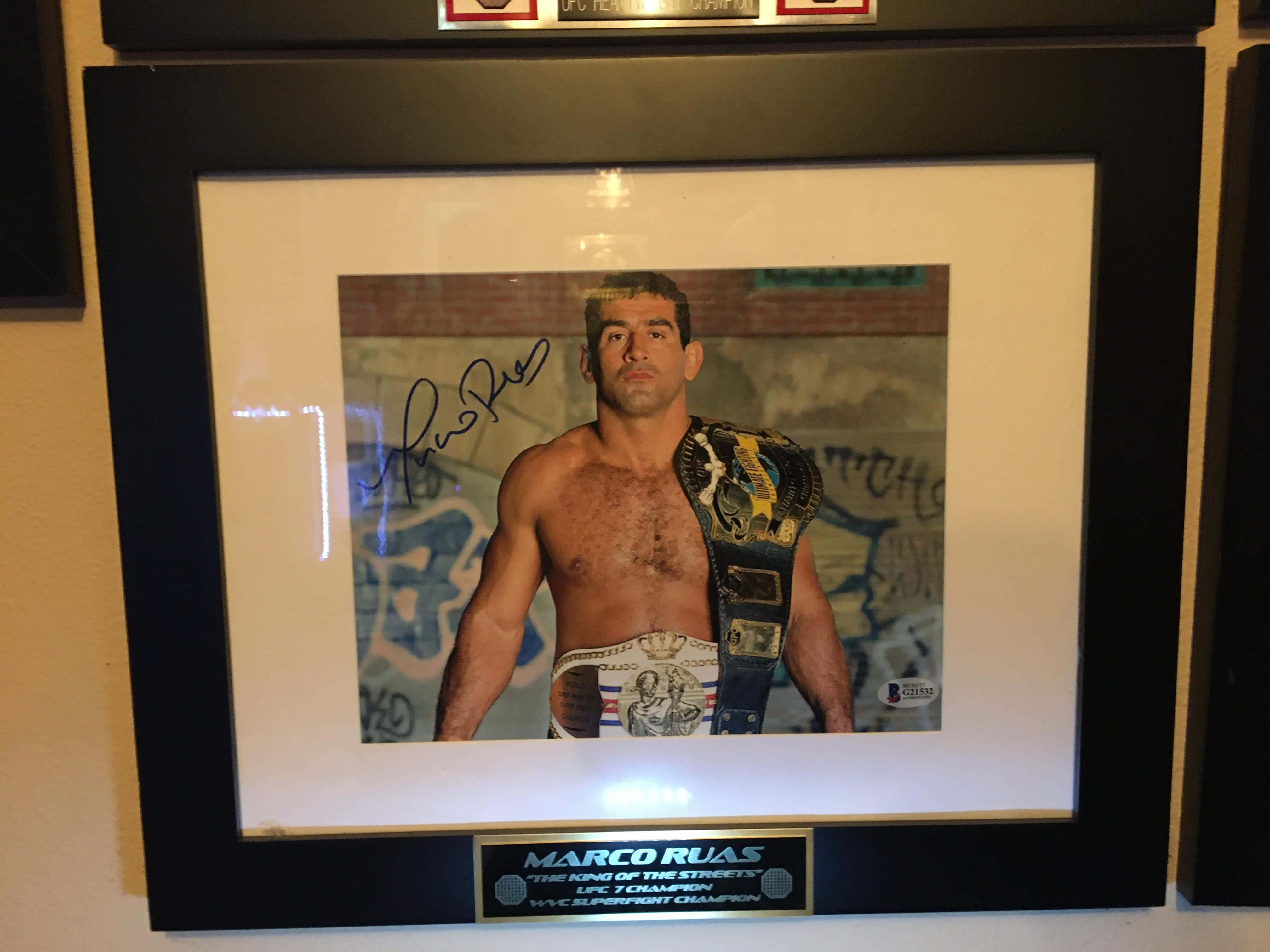 MMA 桌布 壁紙 — 一幅裱框的簽名照片，顯示拳手 Marco Ruas 在塗鴉牆背景下佩戴冠軍腰帶。