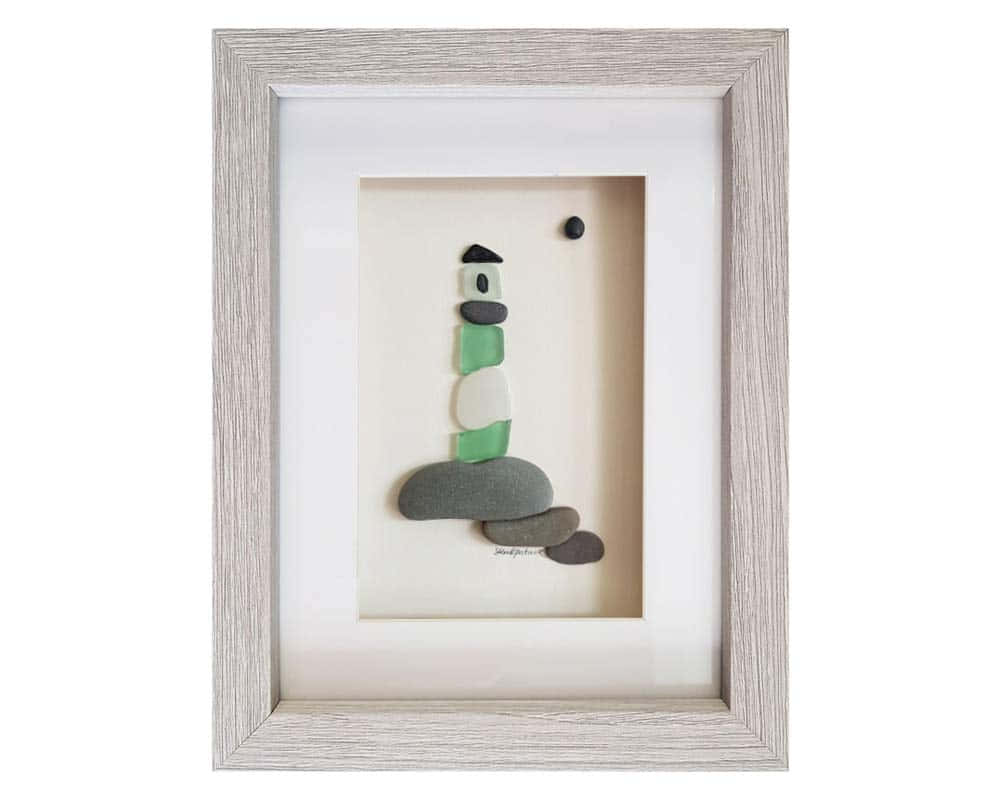 Sea Glass 桌布 壁紙 — 一幅裱框藝術品，由光滑的石頭排列成燈塔輪廓，背景為米色。