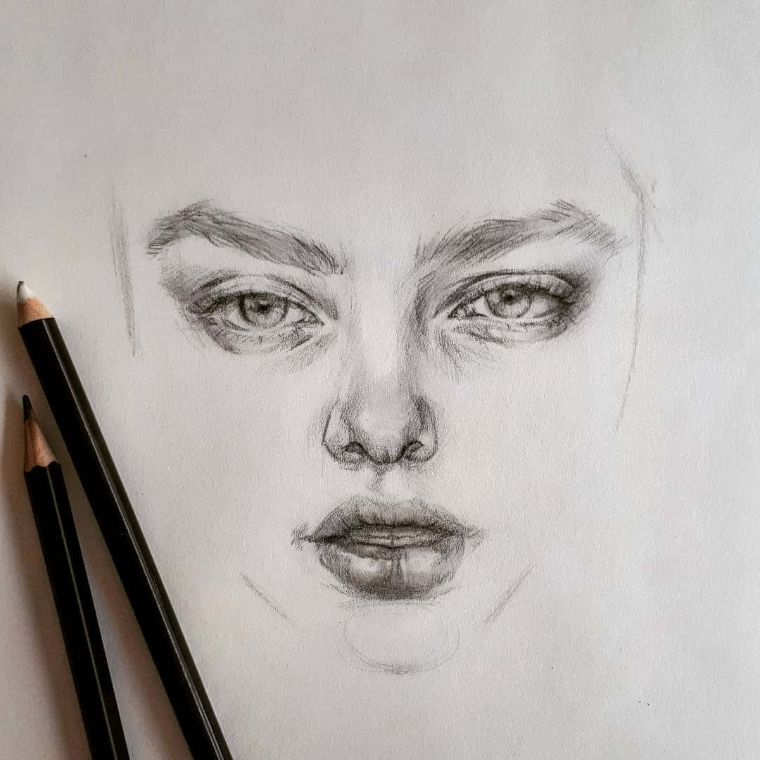 Face 桌布 壁紙 — 一幅詳細的鉛筆素描，描繪一位擁有強烈眼神和嘴唇的女性面孔，兩支鉛筆放在旁邊的紋理紙上。