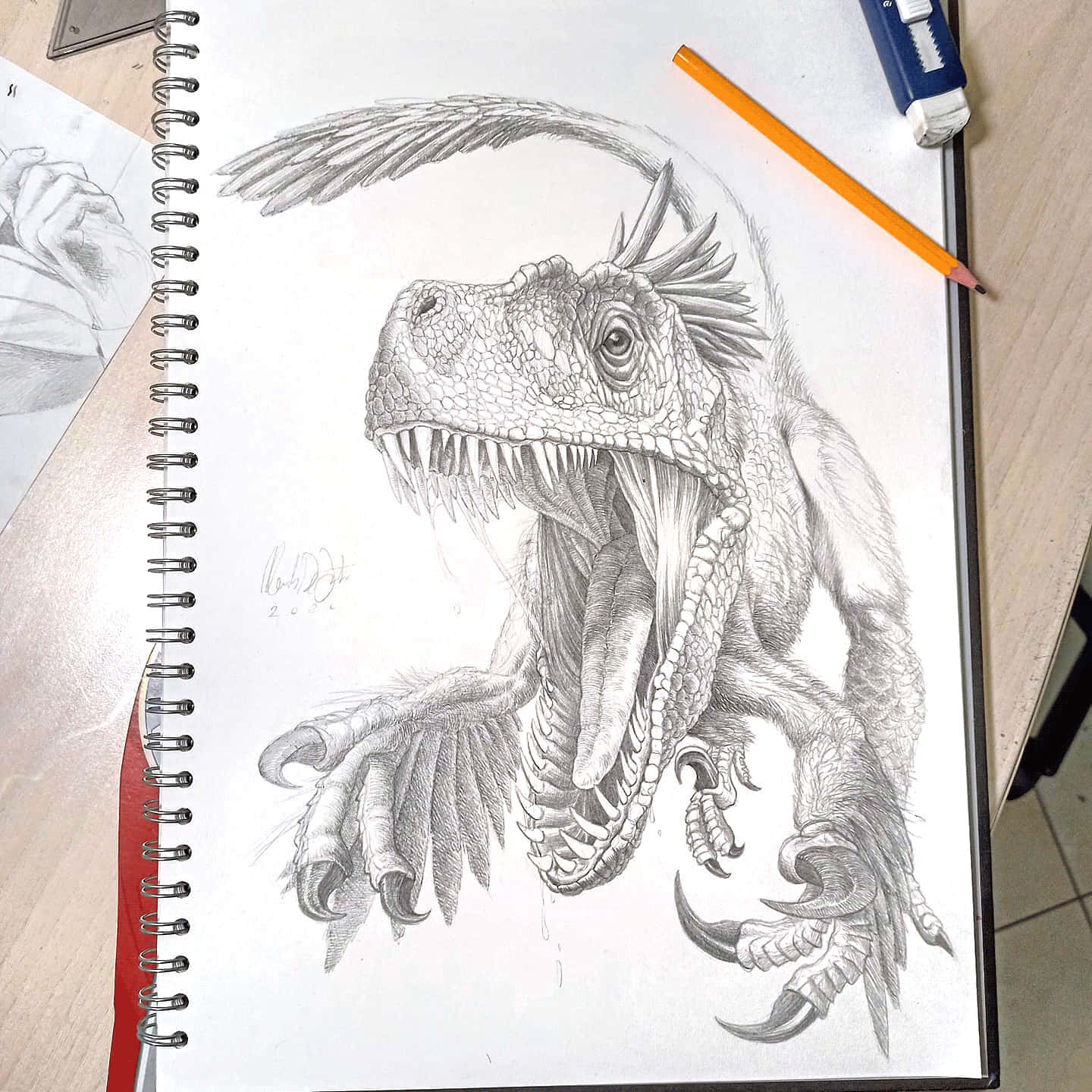 Dinosaur Drawing 桌布 壁紙 — 一幅詳細的鉛筆素描，描繪一隻兇猛、有羽毛的恐龍，擁有鋒利的牙齒和爪子，畫在素描本中，旁邊有一支橙色鉛筆。