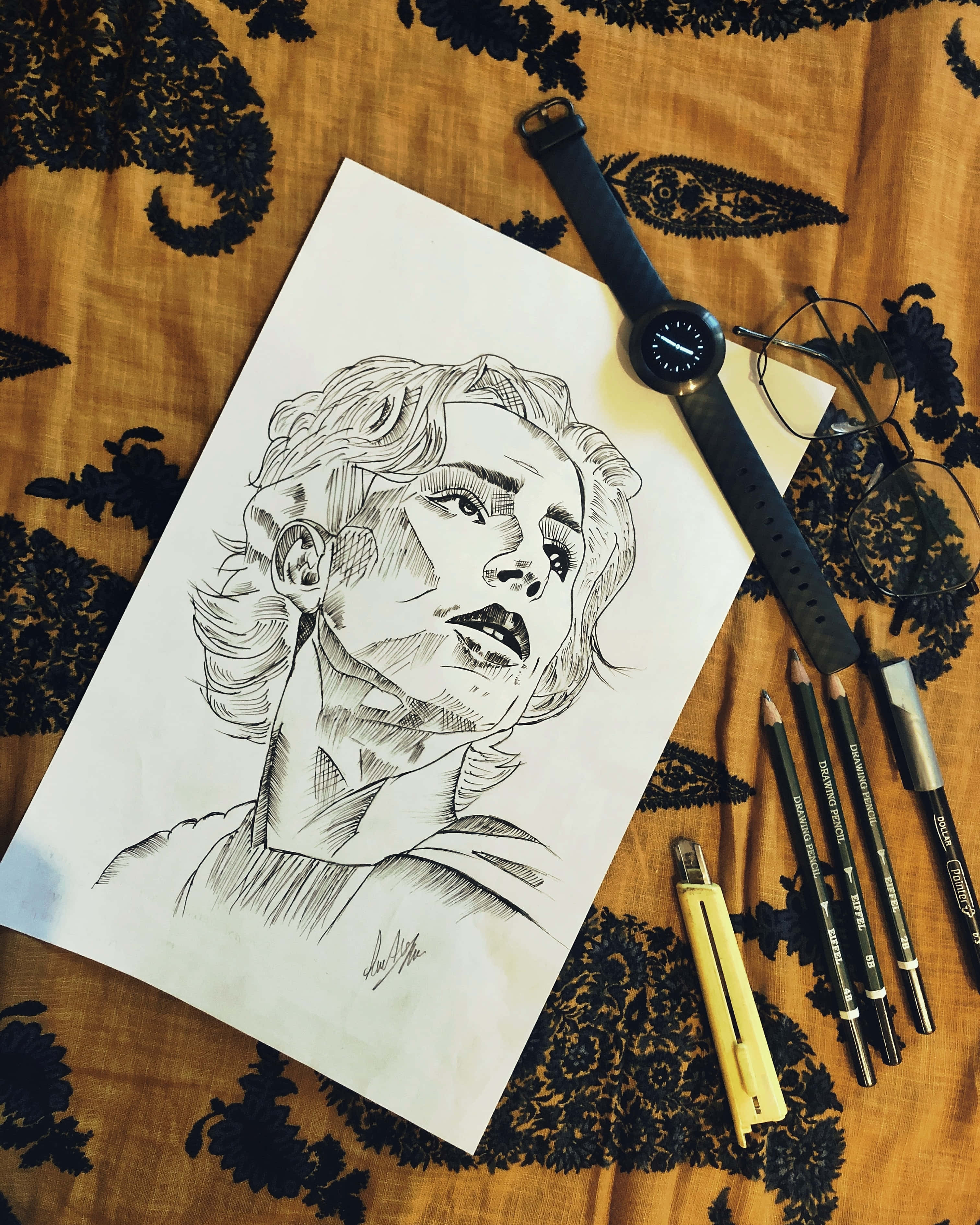 繪畫 桌布 壁紙 — 一幅詳細的黑白鉛筆素描，描繪一個人的臉部，放在有圖案的布料上，旁邊有繪畫工具和智慧手錶。