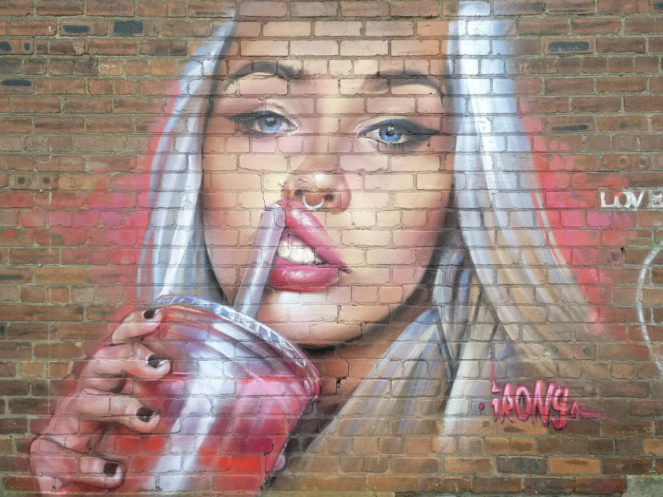 Graffiti Art 桌布 壁紙 — 一幅超寫實壁畫，描繪一位藍眼睛的女性在風化的磚牆前用吸管啜飲紅色飲料。