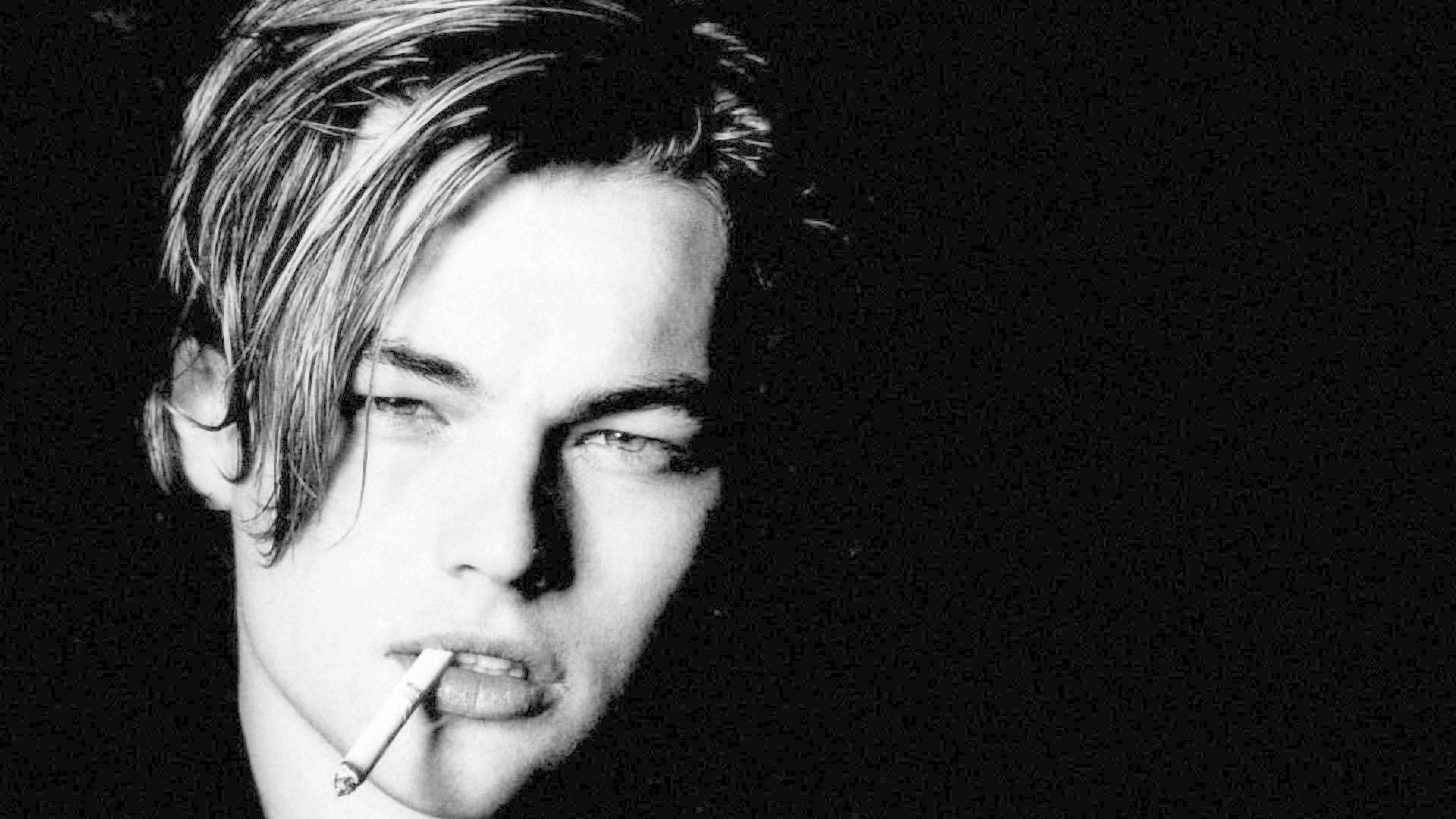Dicaprio 桌布 壁紙 — 一幅陰鬱的黑白肖像，描繪一位頭髮凌亂的年輕男子，在黑暗背景前嘴裡叼著香煙。