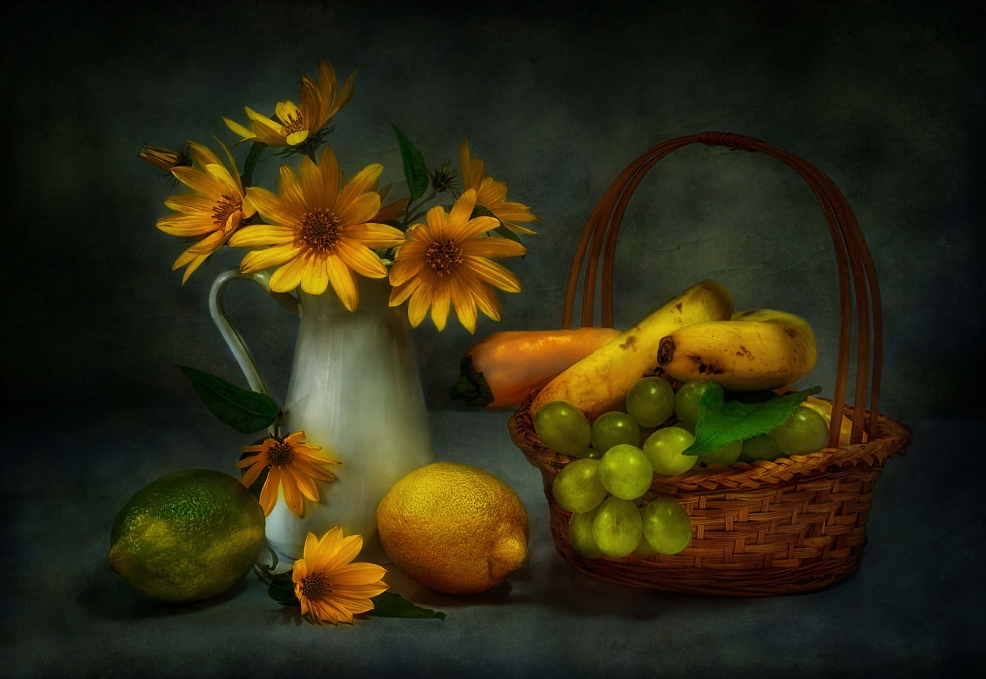 Fruits 桌布 壁紙 — 一幅靜物畫，描繪白色水壺中的向日葵，旁邊放著一個裝滿葡萄、香蕉和柑橘類水果的柳條籃子，背景為深色紋理。