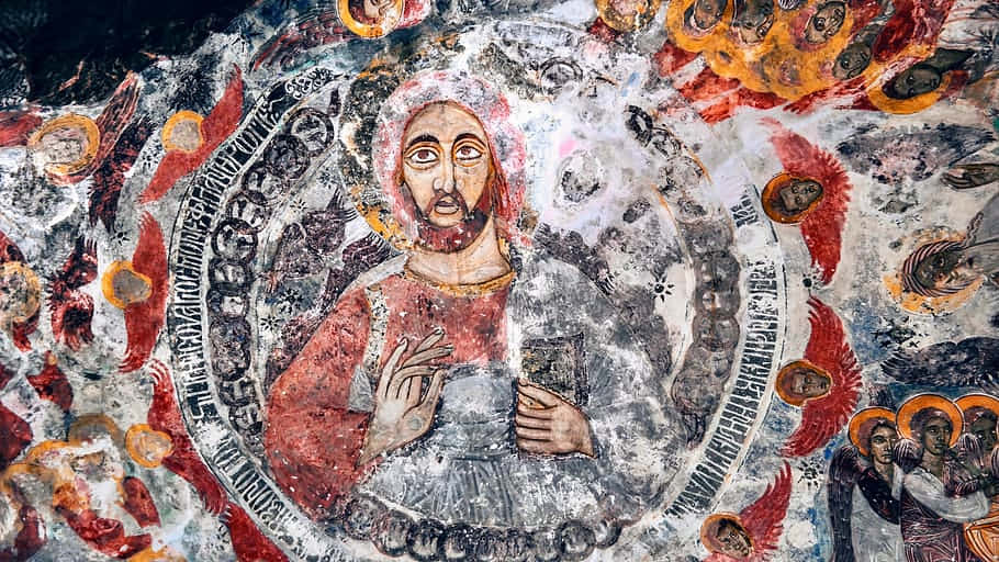 Religious Art 桌布 壁紙 — 一幅風化的古代壁畫描繪了一位中央留鬍鬚的人物，身穿紅白長袍，手持一本書，周圍環繞著天使和西里爾字母。