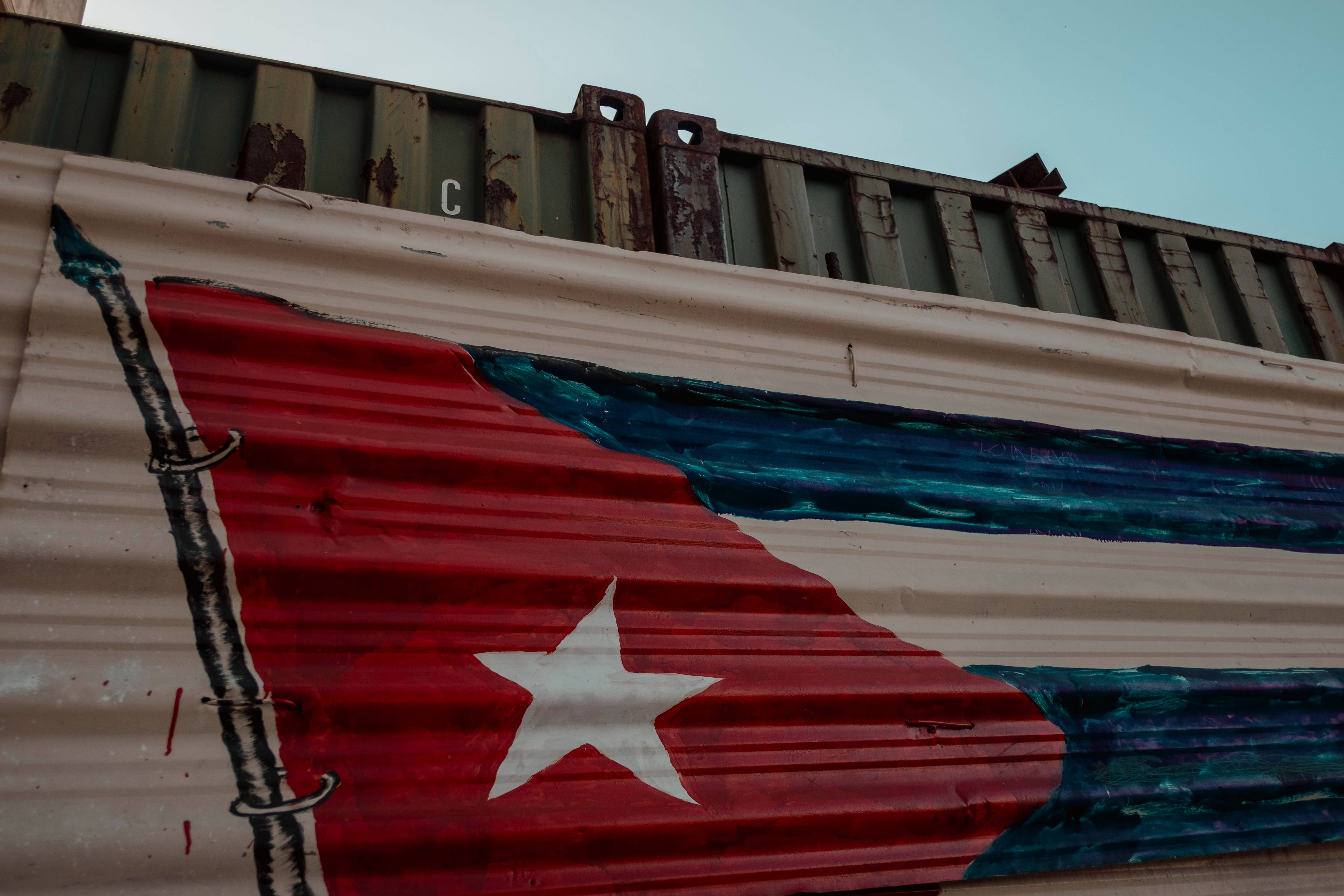 Cuban 桌布 壁紙 — 一幅飽經風霜的古巴國旗，畫在波紋金屬板上，背景有一個生鏽的貨運貨櫃。