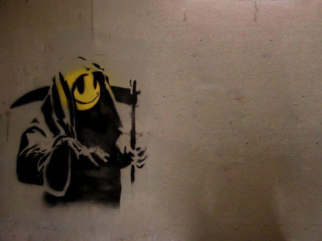 Banksy 桌布 壁紙 — 一幅鮮明的塗鴉壁畫，描繪了一個戴著黃色笑臉兜帽的死神，手持鐮刀，位於紋理牆壁上。