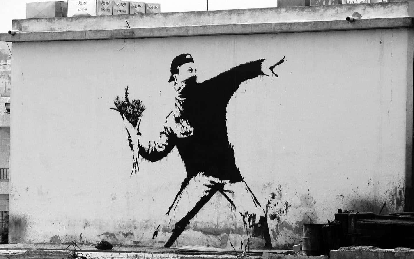 Banksy 桌布 壁紙 — 一幅鮮明的黑白壁畫，描繪一個戴帽的人物在風化的城市牆上，手持花束並拋擲花朵。