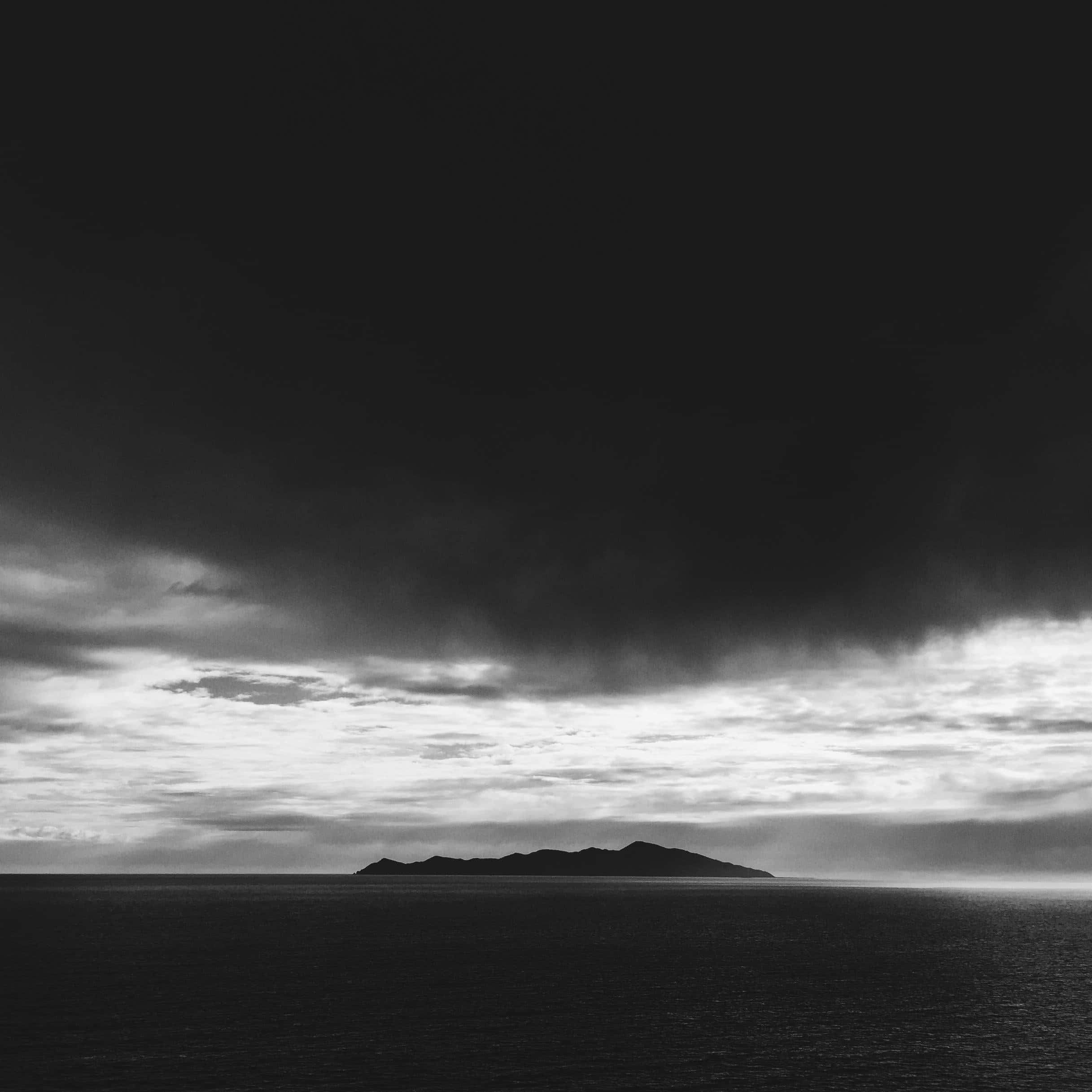Black And White Storm 桌布 壁紙 — 一幅鮮明的黑白海景，顯示在厚重暴風雲層下遠處島嶼的輪廓。