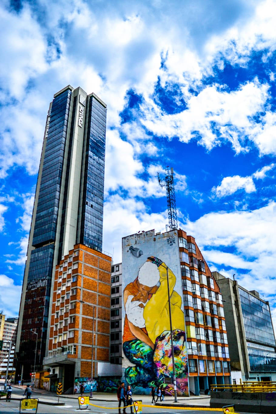 Bogota 桌布 壁紙 — 一幅黃色和綠色人物的鮮豔壁畫，點綴著建築物，背景是明亮的藍天和蓬鬆的白雲。
