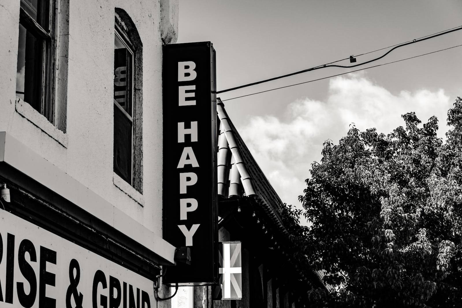 Motivation 桌布 壁紙 — 一幅黑白城市街景，建築物上有垂直的「BE HAPPY」標誌，建築物有拱形窗戶和一棵樹。