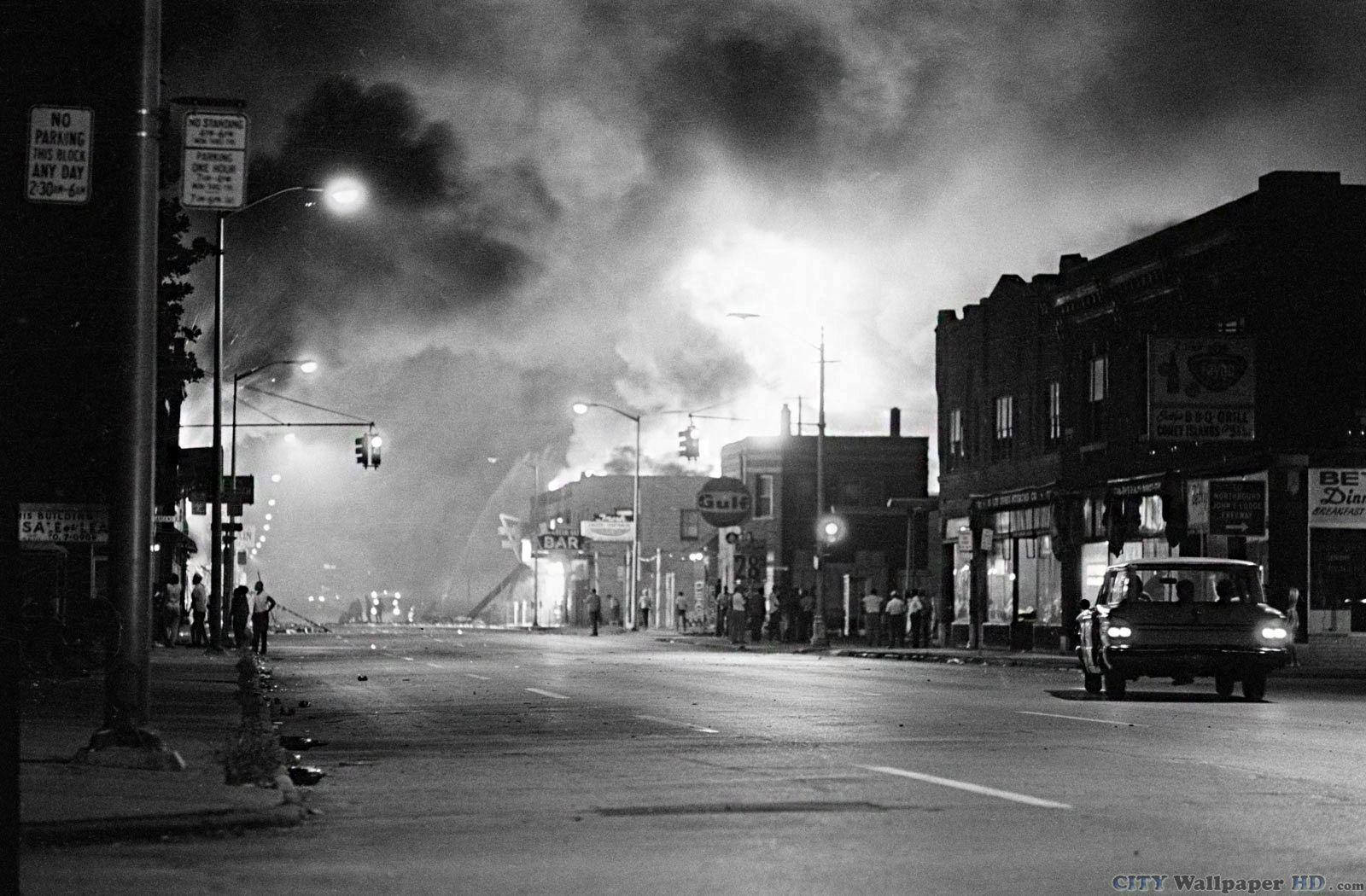 detroit 桌布 壁紙 — 一幅黑白夜景街道場景，遠方火災冒煙，人群聚集，一輛汽車駛過。