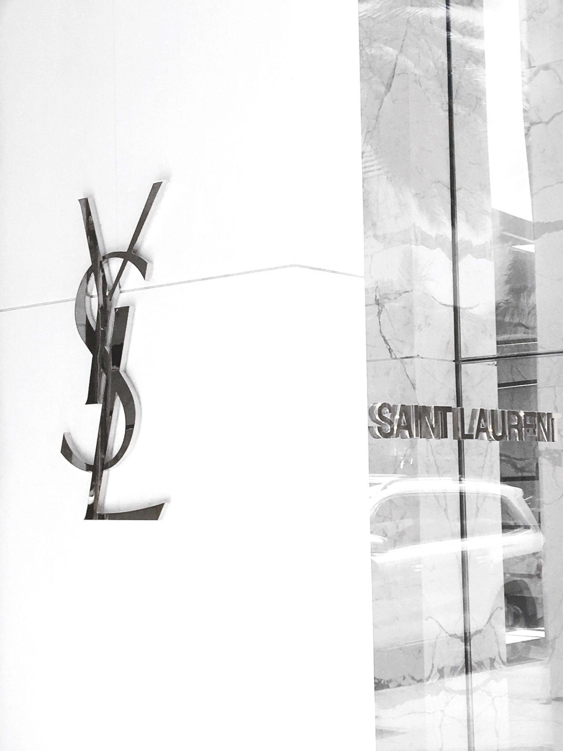 YSL 桌布 壁紙 — 一幅黑白照片，YSL標誌安裝在白色牆壁上，旁邊的玻璃幕牆反射出大理石柱和汽車。