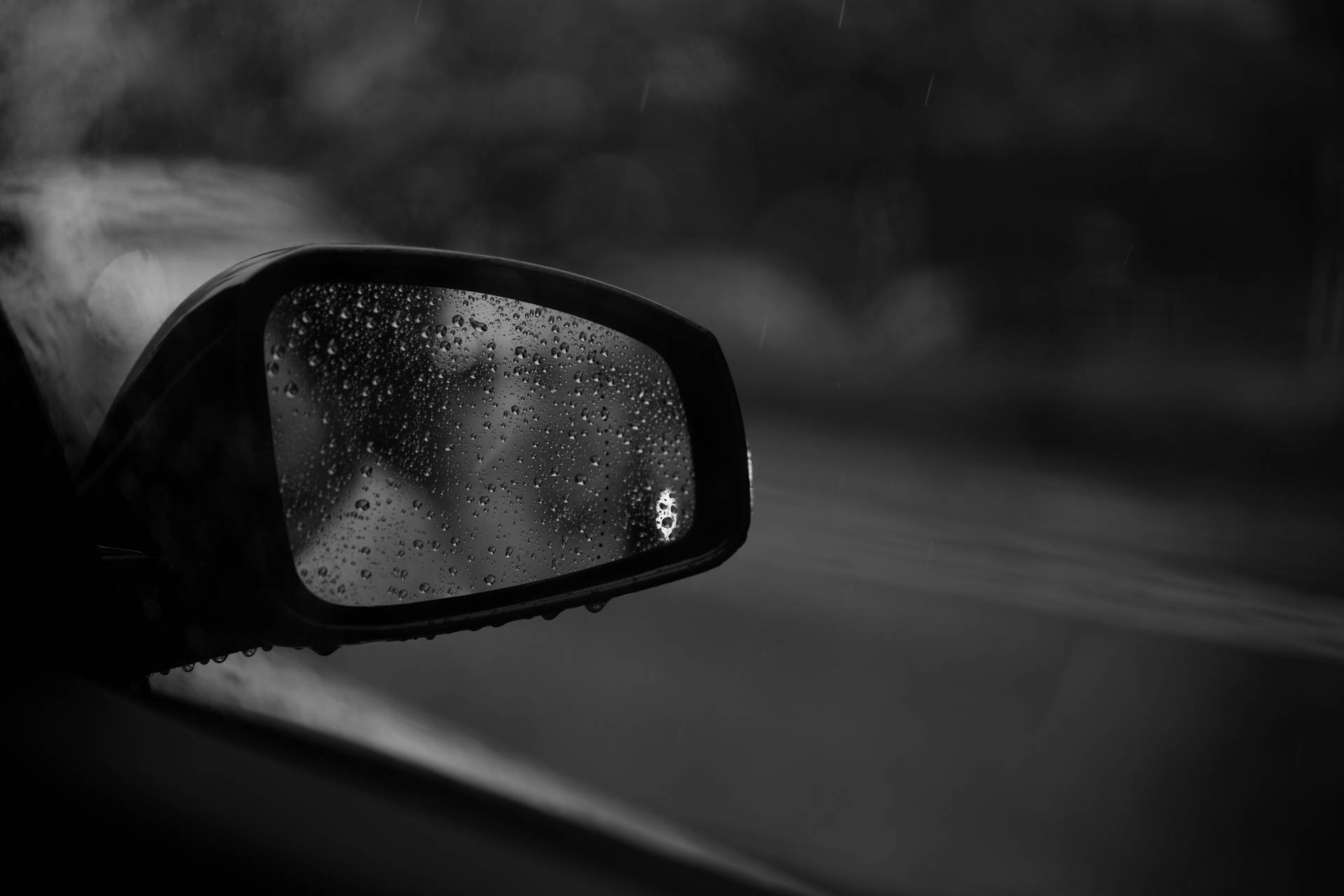 黑白 桌布 壁紙 — 一幅黑白特寫，展示沾滿雨點的汽車側鏡，在濕滑路面上反射出模糊的動態。