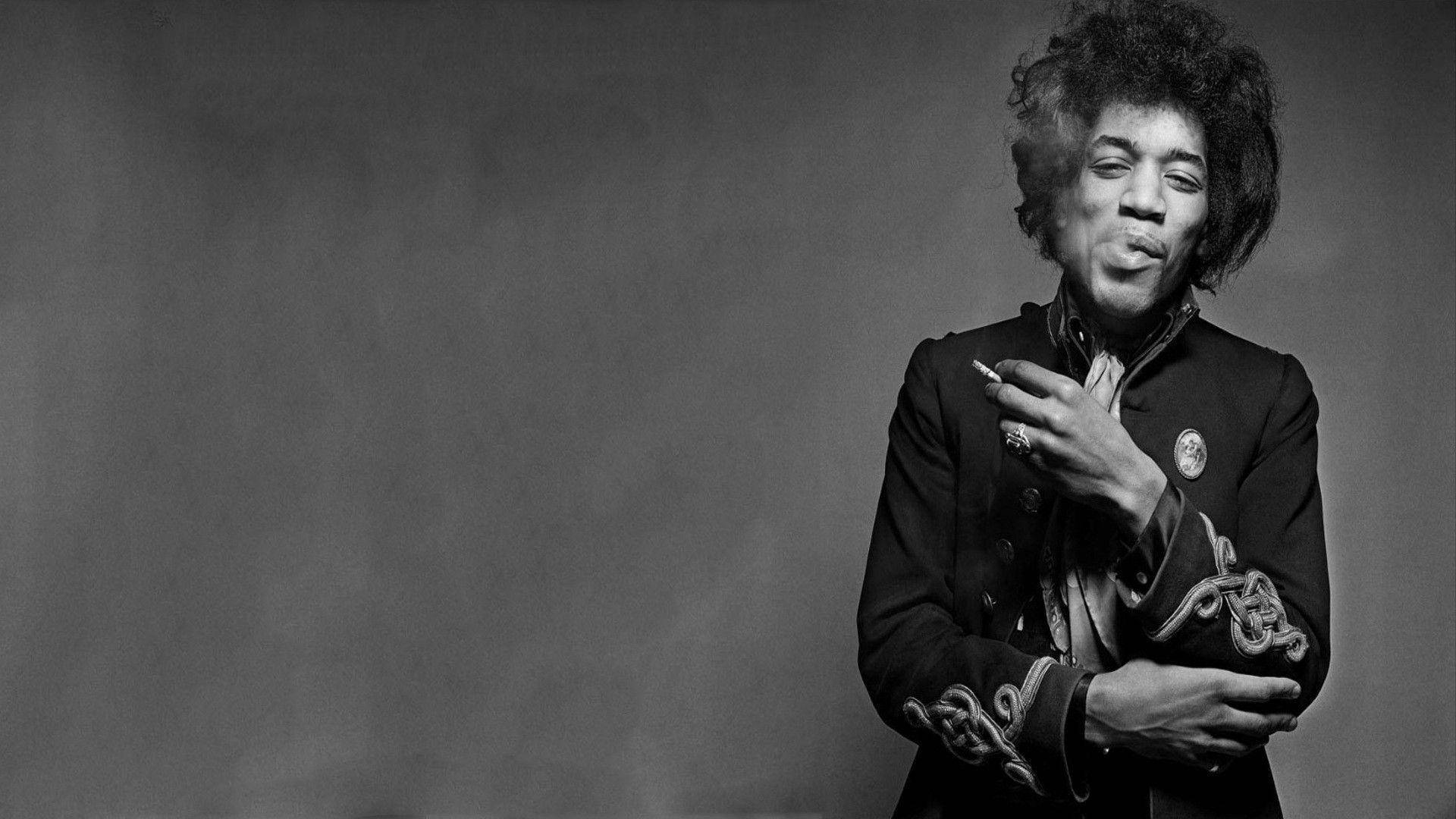 黑白 桌布 壁紙 — 一幅黑白肖像，Jimi Hendrix 在煙霧瀰漫的灰色背景下抽煙，帶著頑皮的微笑。