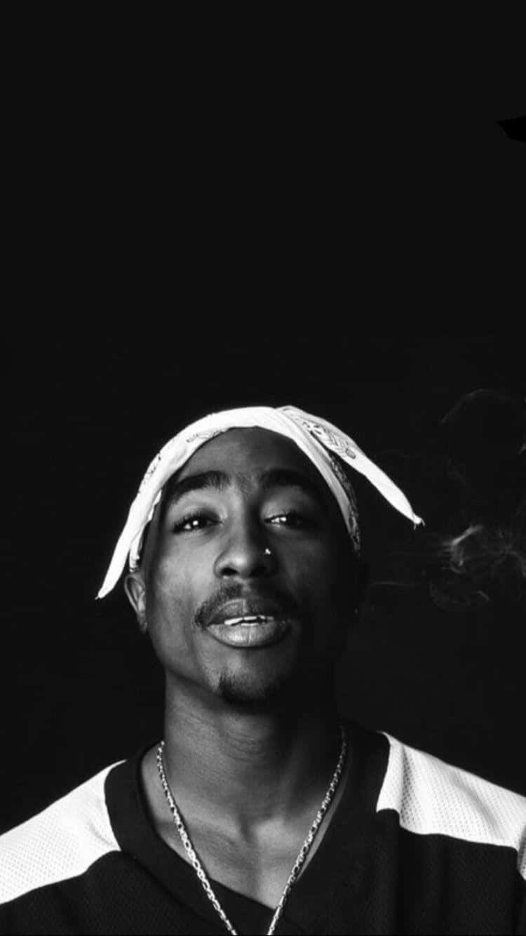 Tupac iPhone 桌布 壁紙 — 一幅黑白肖像，Tupac Shakur 在黑暗背景中輕柔微笑，同時抽著香煙。