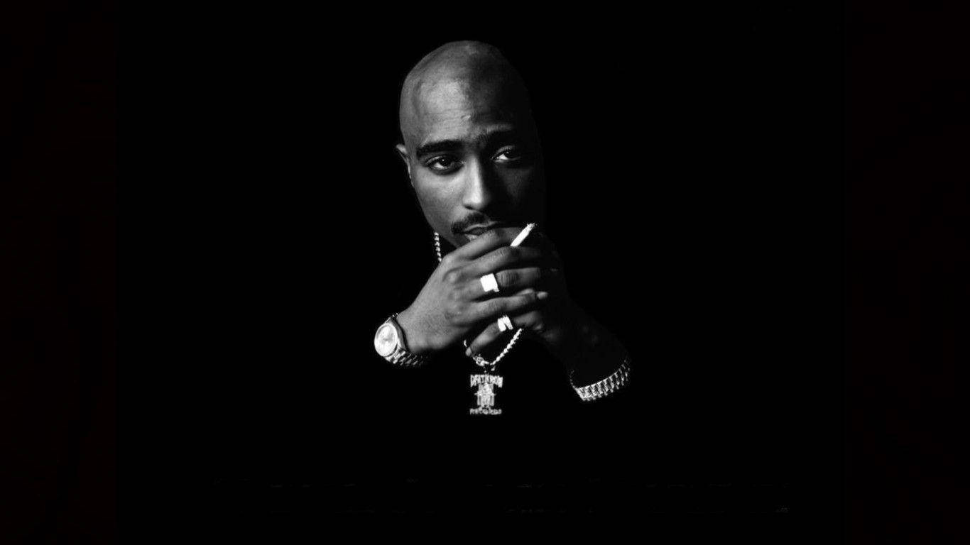tupac 桌布 壁紙 — 一幅黑白肖像，Tupac Shakur 手持香菸，背景陰暗，燈光戲劇化。