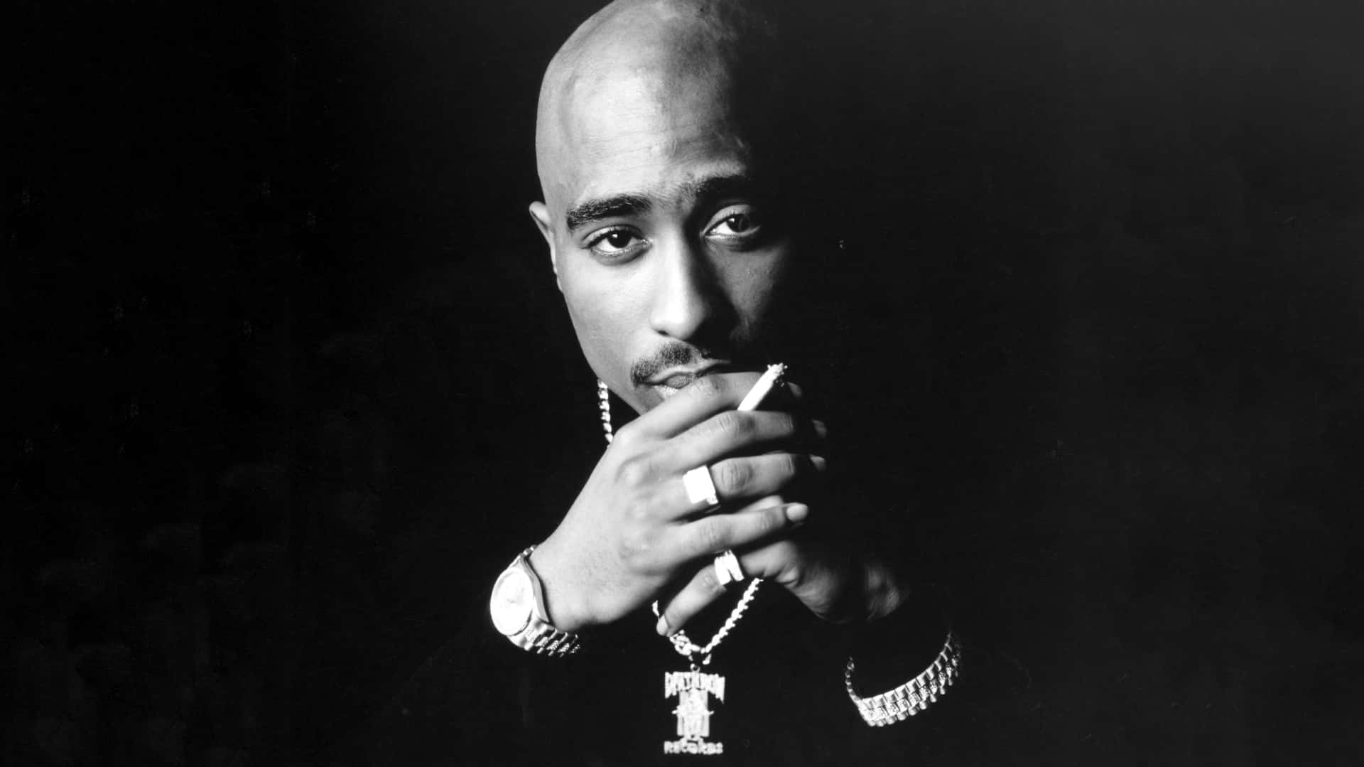 tupac 桌布 壁紙 — 一幅黑白肖像，Tupac Shakur 手持香菸，神情嚴肅，背景昏暗。