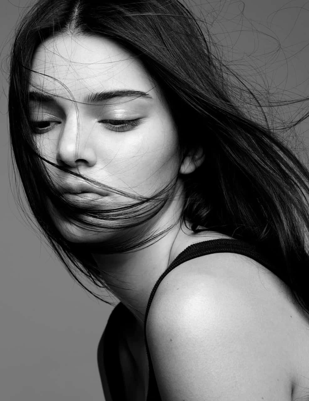 Black And White Celebrity 桌布 壁紙 — 一幅黑白肖像，一位女性被風吹亂的頭髮部分遮蓋了她的臉，背景是純灰色。