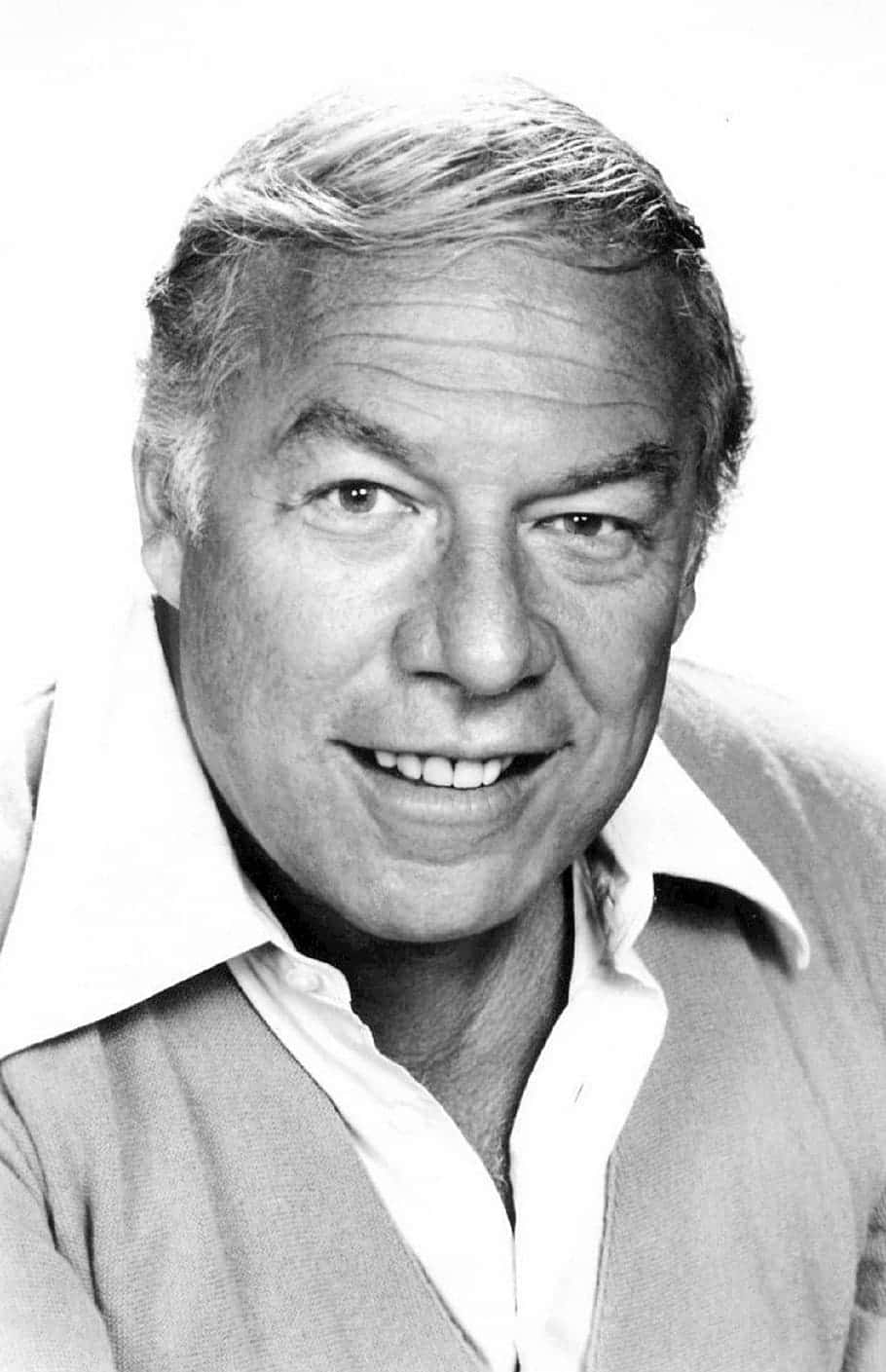 George Kennedy 桌布 壁紙 — 一幅黑白肖像，一位微笑的中年灰髮男子穿著有領襯衫和毛衣背心。