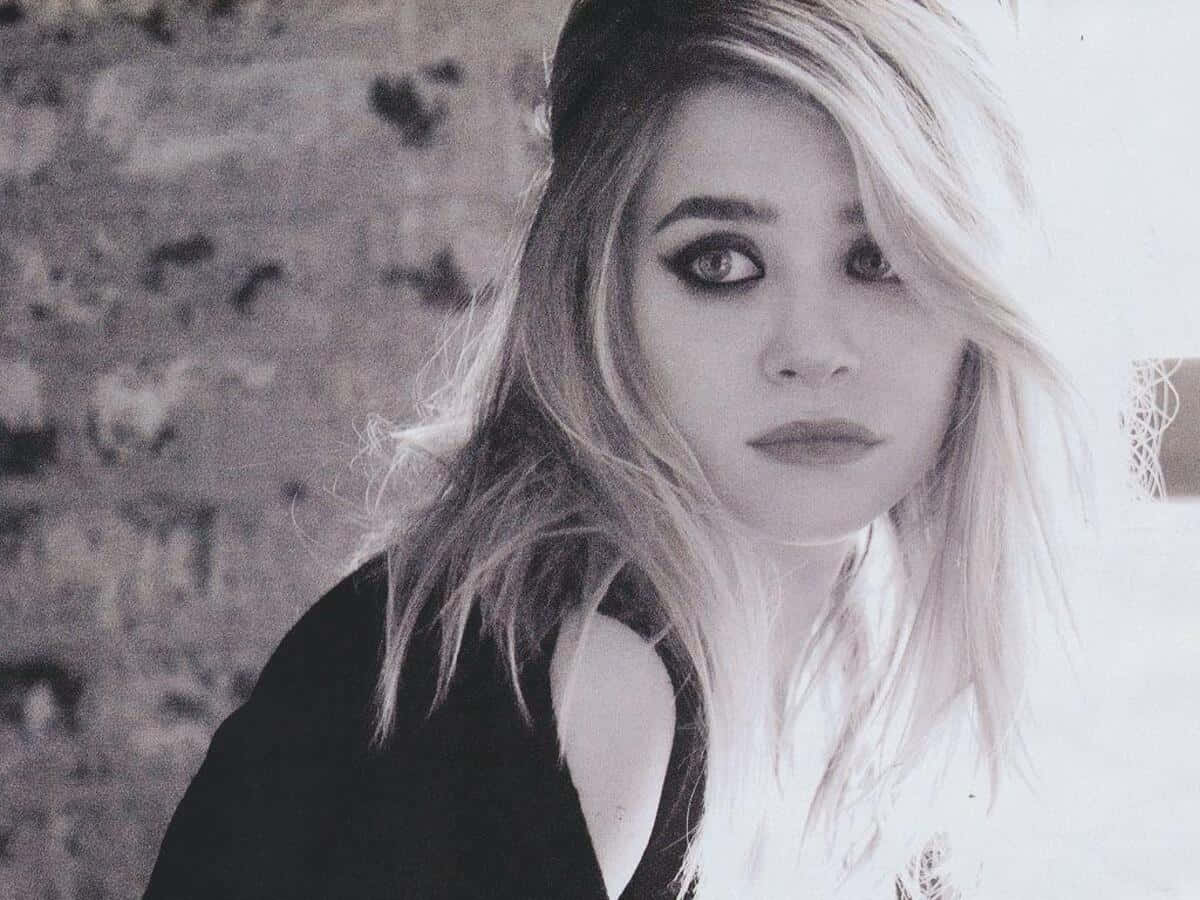 Mary Kate Olsen 桌布 壁紙 — 一幅黑白肖像，一位頭髮凌亂的金髮女子，眼神銳利，背景是質感石牆。