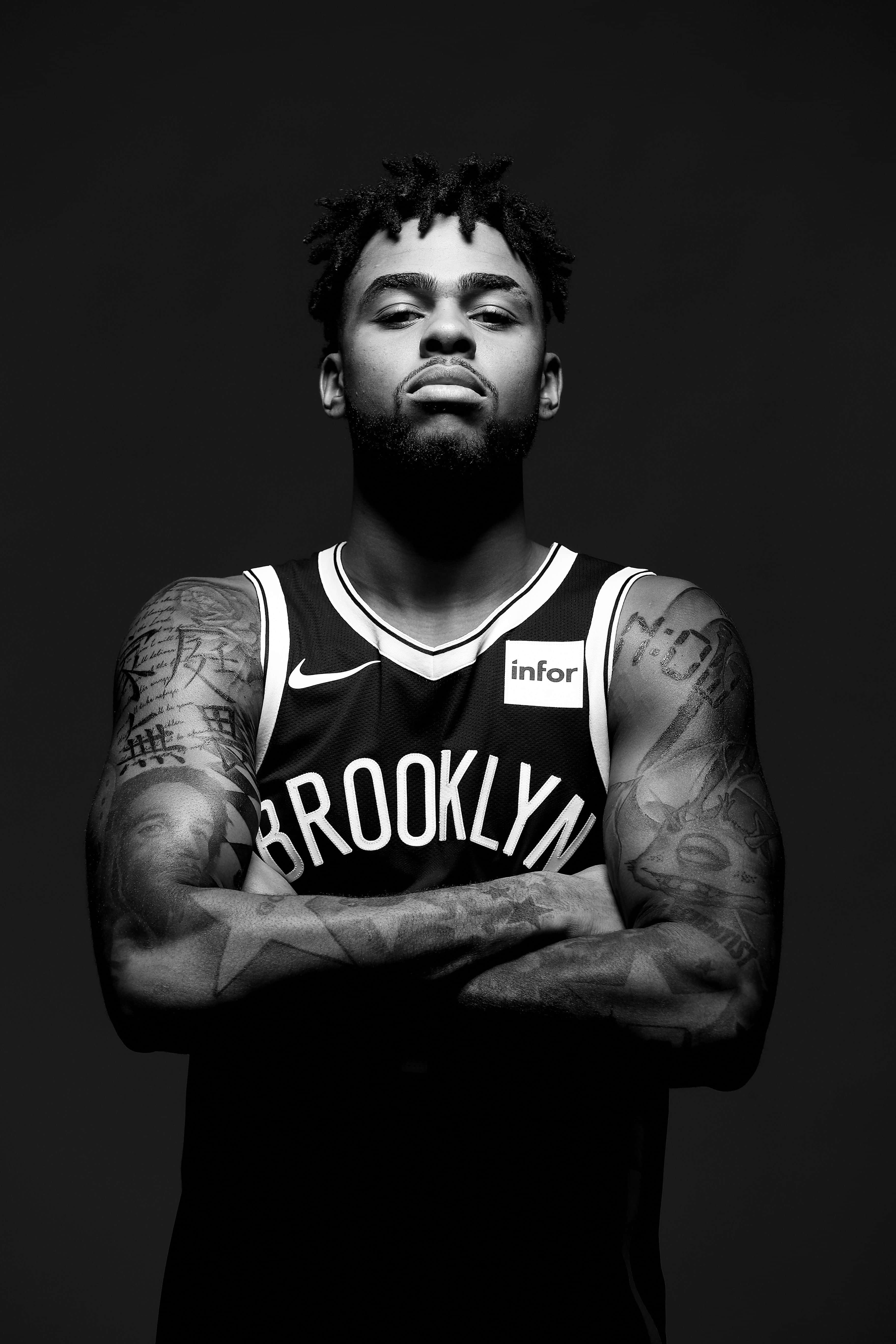Dangelo Russell 桌布 壁紙 — 一幅黑白肖像，展示一位刺青籃球運動員身穿布魯克林球衣，雙臂交叉站在深色背景前。
