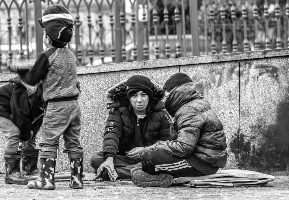 黑白 桌布 壁紙 — 一幅黑白街景，顯示一名女子和兩個孩子坐在人行道上，靠近石牆和華麗的圍欄。