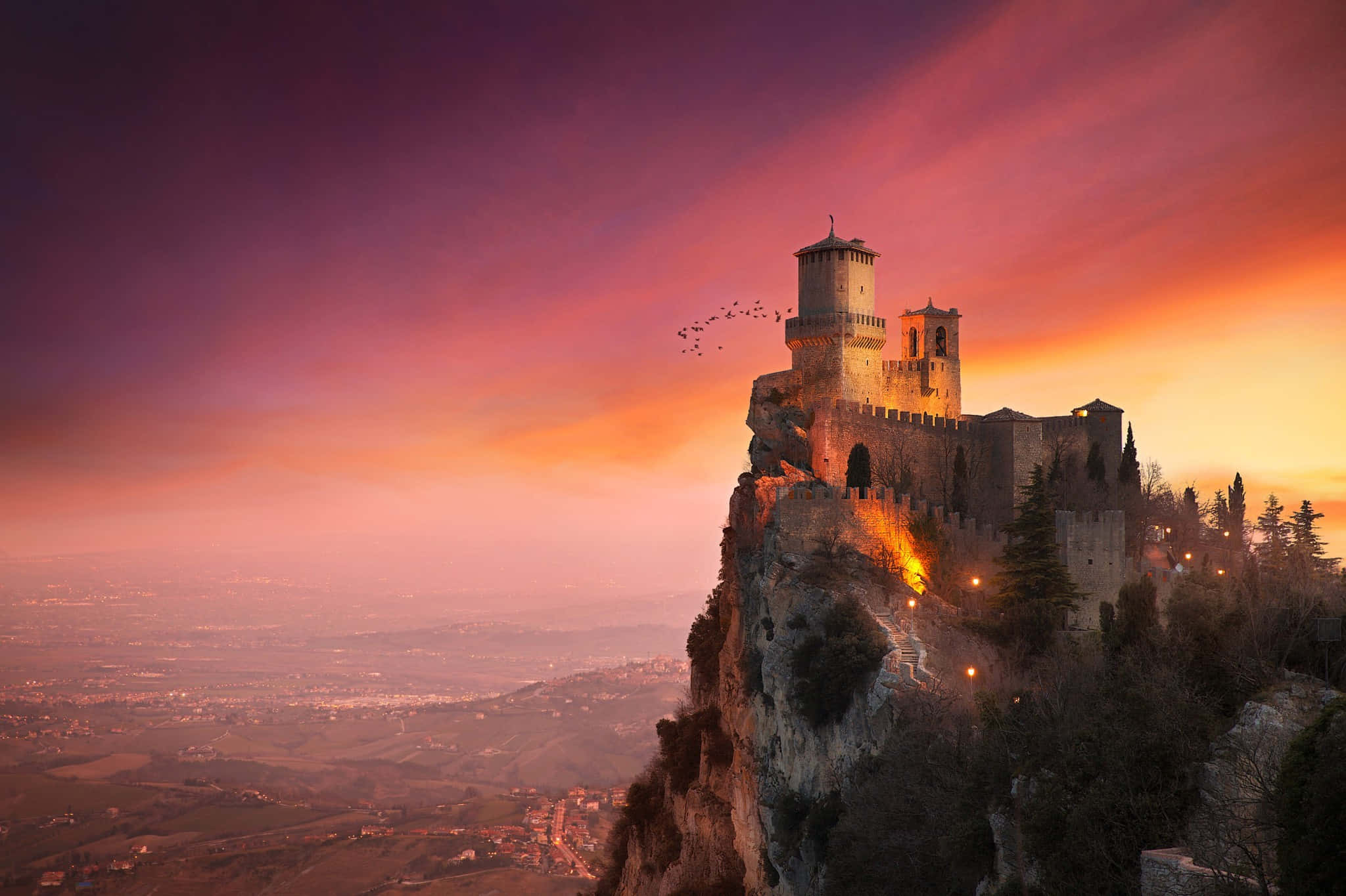 tower 桌布 壁紙 — 一座中世紀城堡坐落在懸崖上，夕陽西下，上方是火橙色和紫色的天空。