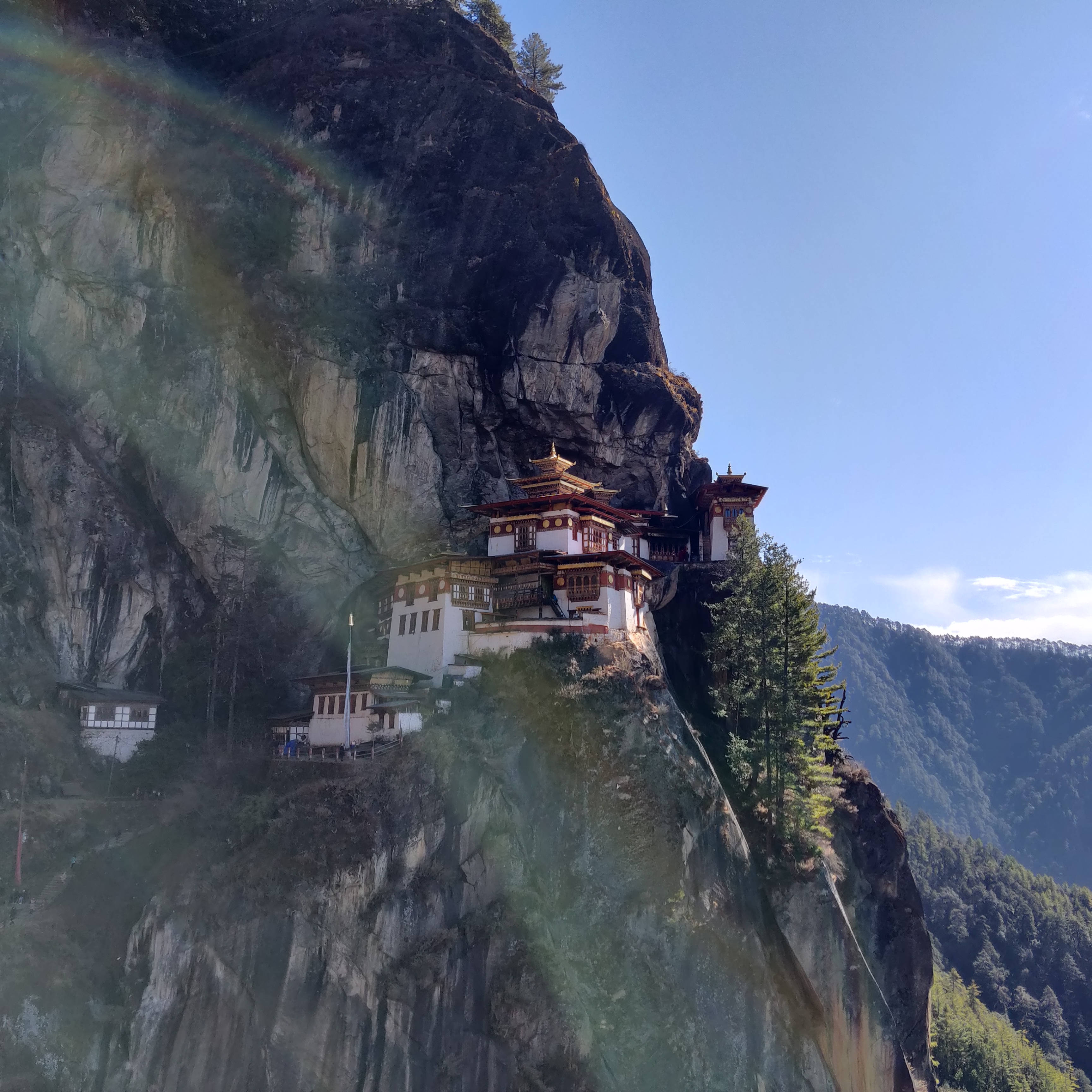 Bhutan 桌布 壁紙 — 一座令人驚嘆的佛教寺院緊貼在陡峭的懸崖面上，上方是清澈的藍天，一道淡淡的彩虹拱起。