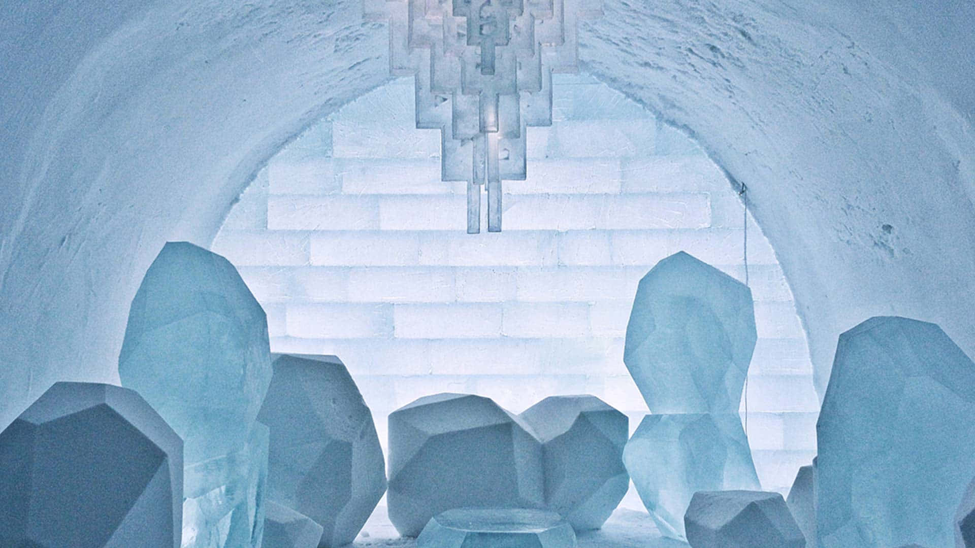 Ice Hotel 桌布 壁紙 — 一座令人驚嘆的冰之大教堂，擁有幾何水晶結構和拱形牆壁，在柔和藍光下閃耀。