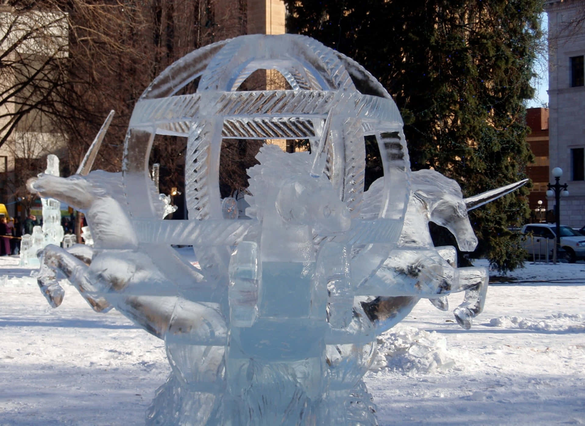 Ice Sculpture 桌布 壁紙 — 一座令人驚嘆的冰雕，描繪由兩隻獨角獸拉著的戰車，矗立在雪白的城市廣場上，沐浴在明亮的日光下。