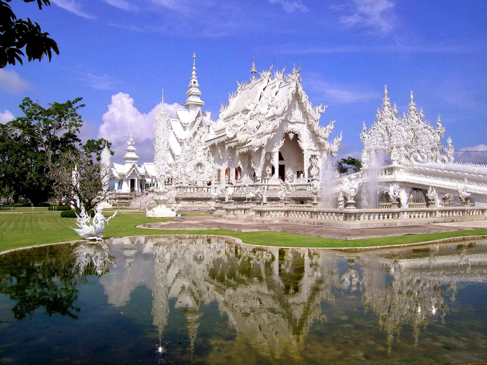 Asia 桌布 壁紙 — 一座令人驚嘆的白色寺廟，擁有精緻的尖頂，在明亮的藍天下完美地倒映在平靜的池塘中。