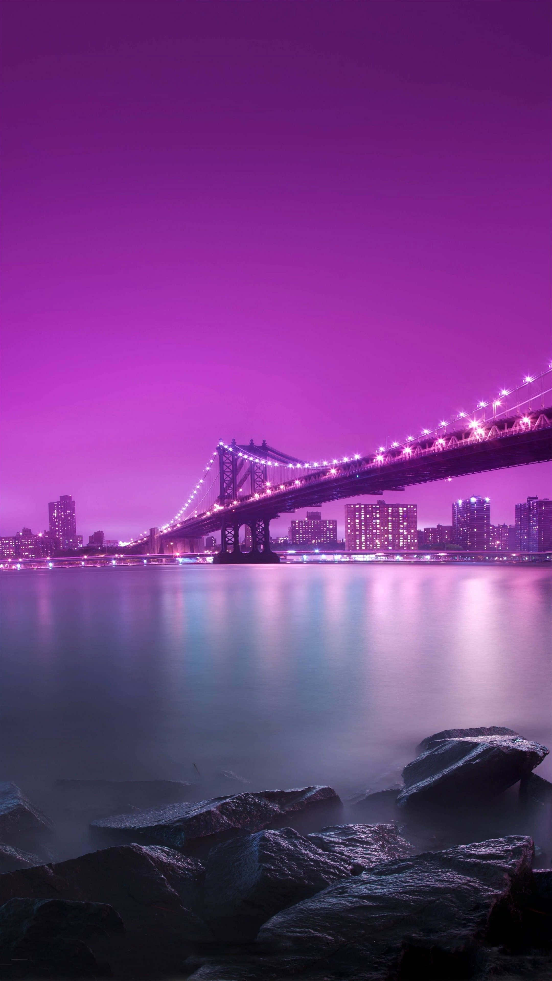 Brooklyn Bridge 桌布 壁紙 — 一座令人驚嘆的紫色橋樑橫跨寧靜的水道，在暮色中，城市燈光倒映在水面下。