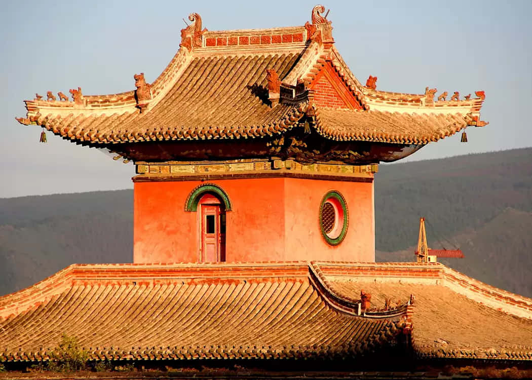 Mongolia 桌布 壁紙 — 一座傳統中國寺廟塔樓，擁有彎曲的瓦頂和華麗的飛簷，在金色時刻矗立於朦朧的山景背景前。