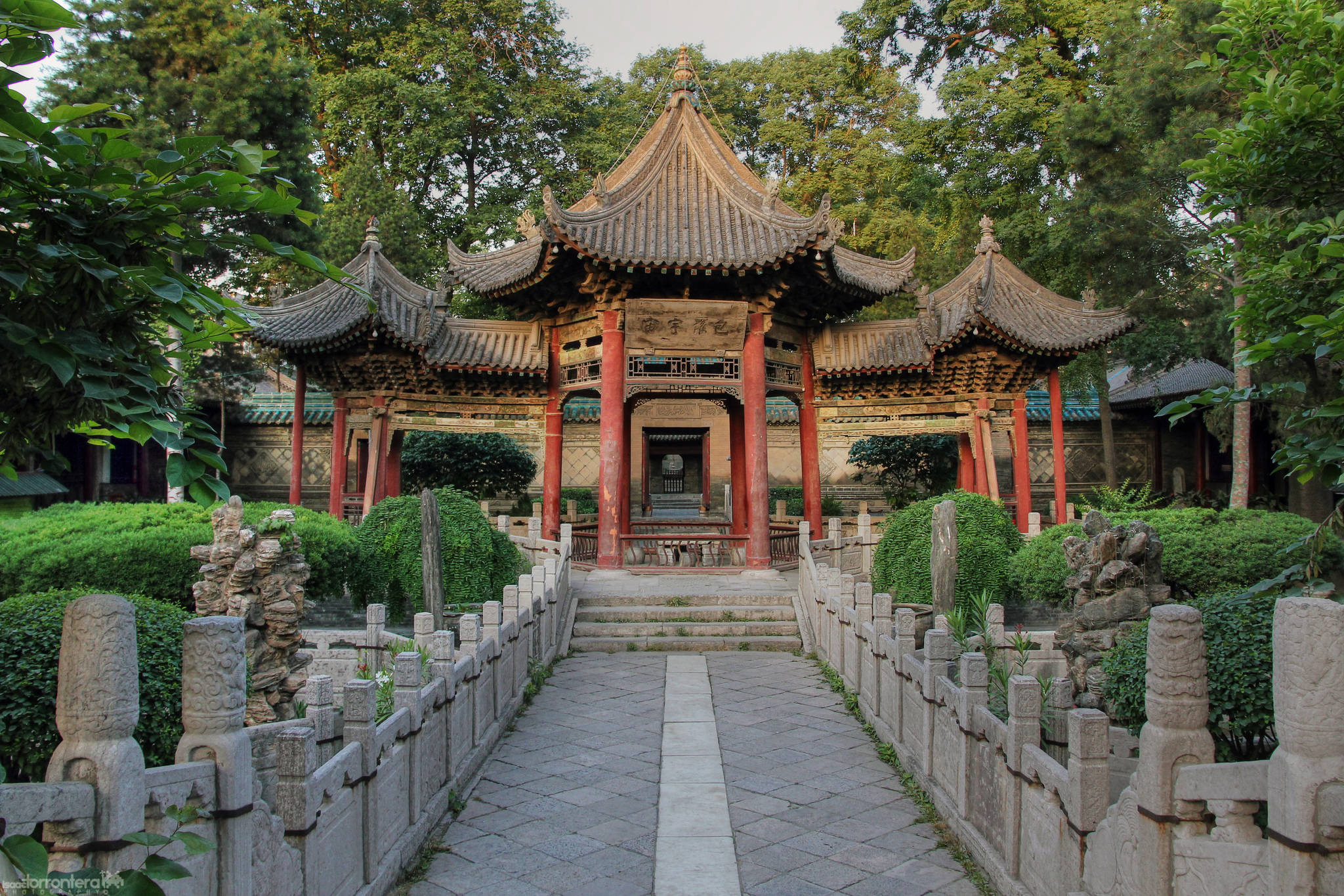 Xian 桌布 壁紙 — 一座傳統中式亭閣，紅柱曲瓦頂，矗立於石徑盡頭，兩旁是修剪整齊的樹籬和古樹。