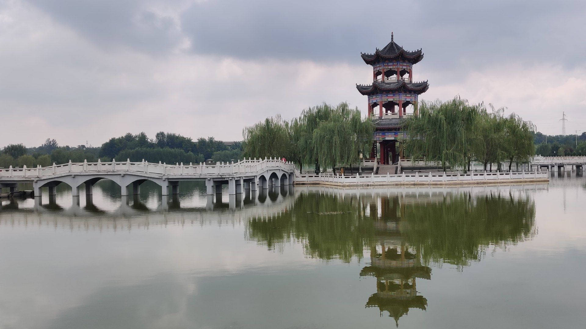 Hangzhou 桌布 壁紙 — 一座傳統中式亭閣和石橋在陰天之下平靜地倒映在寧靜的水面上。
